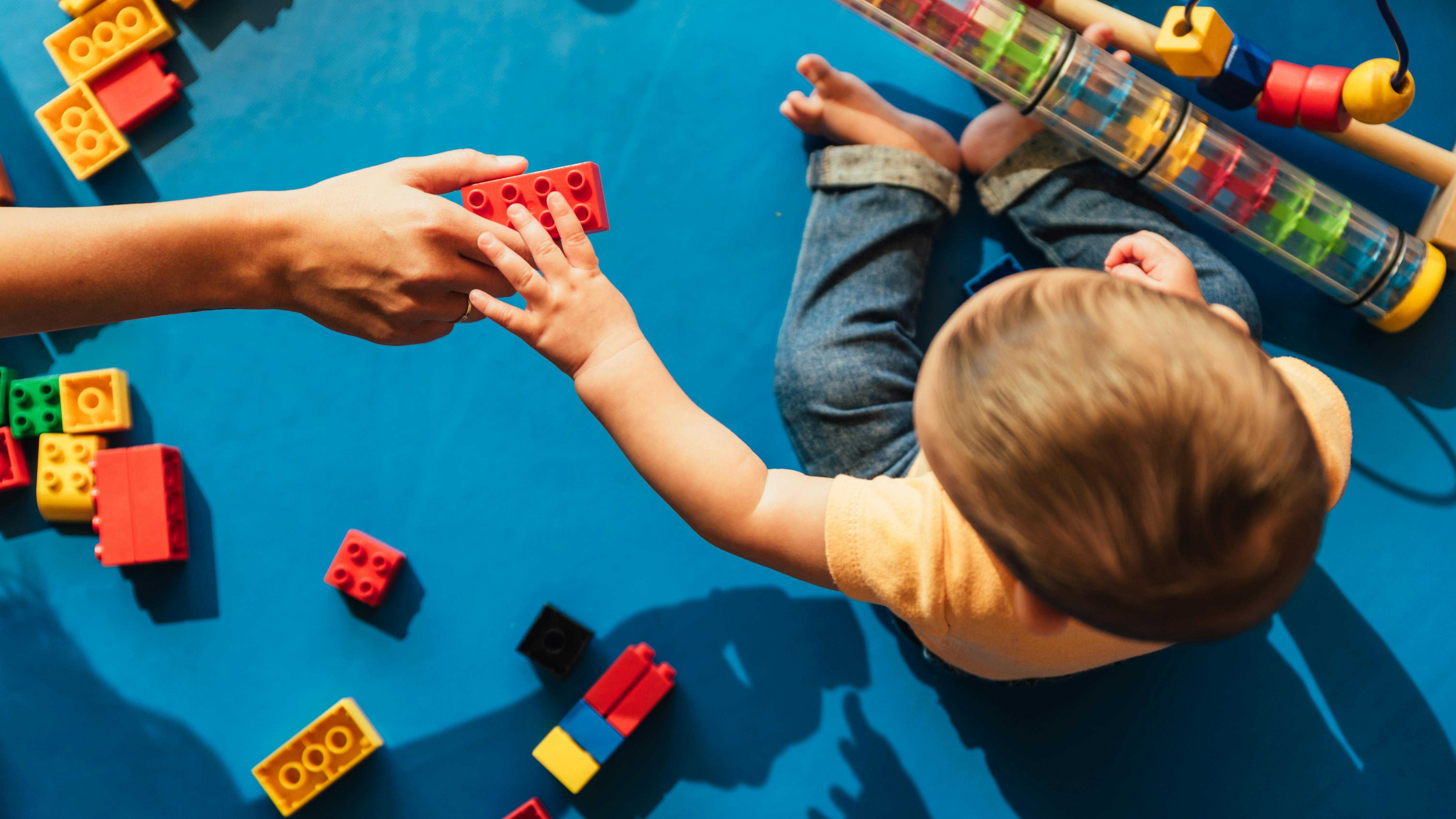 Ein Kindergarten-Kind spielt auf blauem Boden mit Spielklötzen,