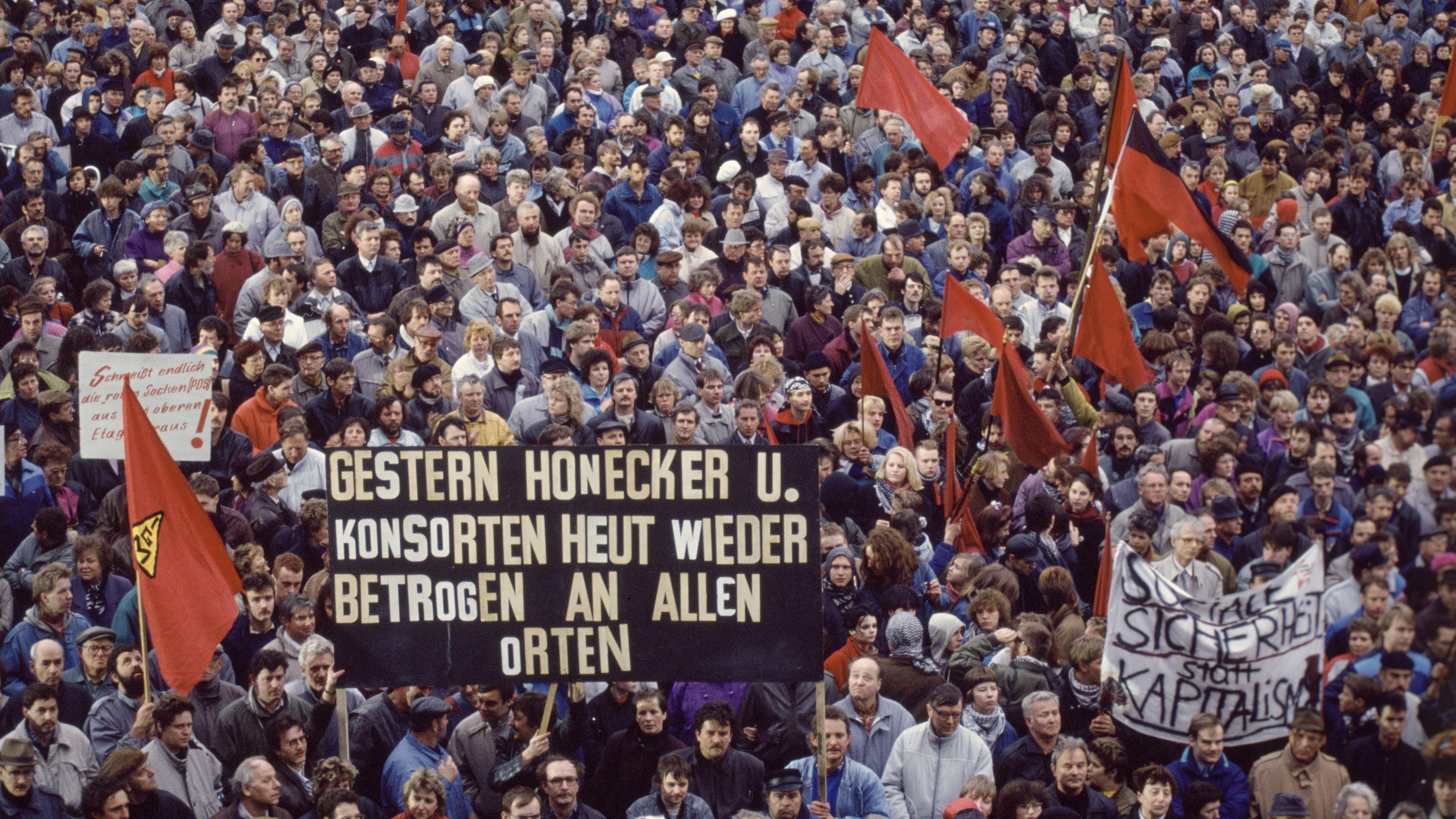 Eine Menschenmenge demonstriert in Leipzig gegen die Krise in Ostdeutschland nach der Wende. Auf dem Plakat im Vordergrund steht: „Gestern Honecker und Konsortien, heut' wieder betrogen an allen Orten“.