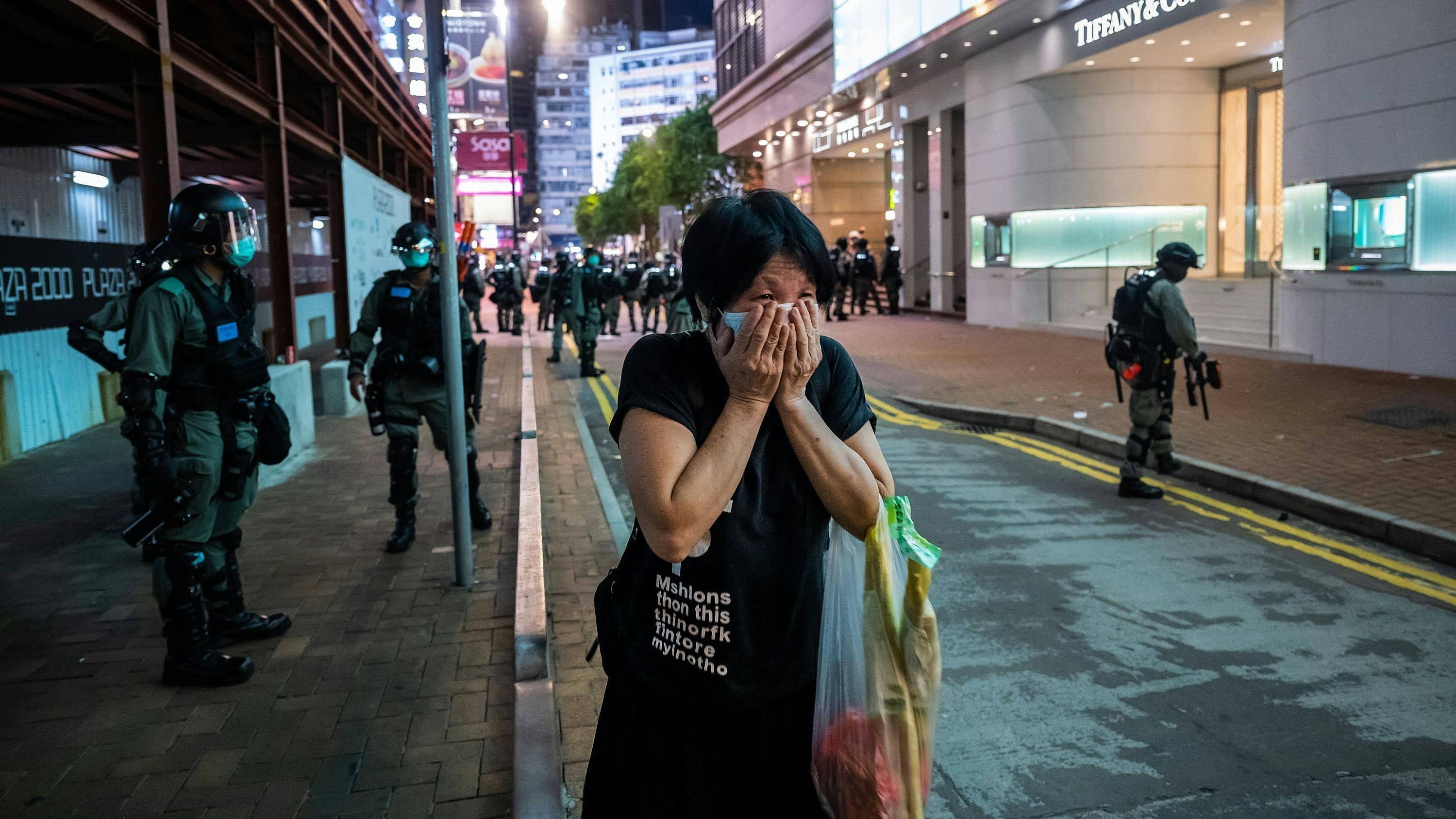 Eine Frau hält sich in den nächtlichen Straßen Hongkongs die Hände vors Gesicht. Hinter ihr stehen Polizisten. 