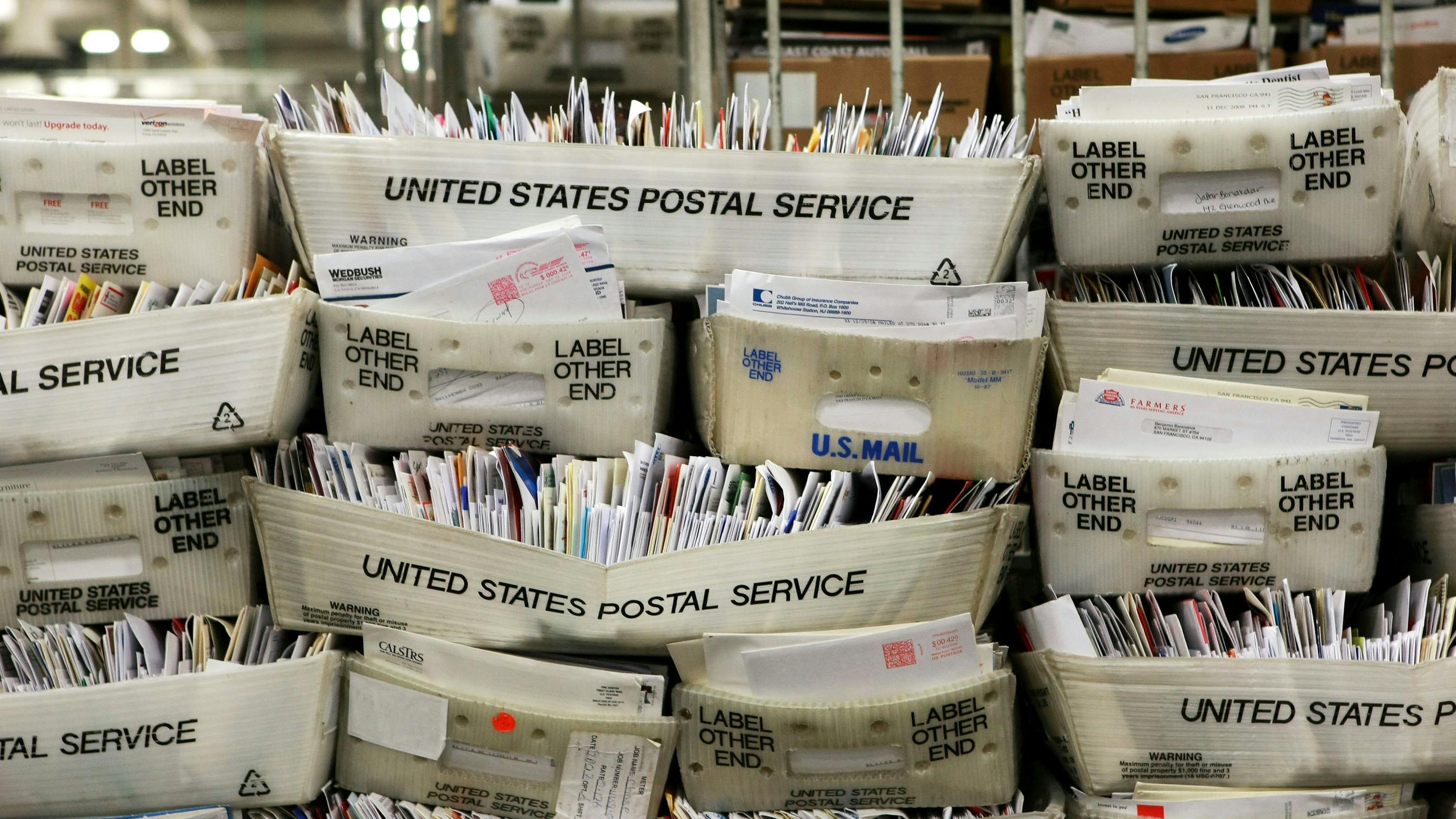Wir sehen einige Kisten voll mit Briefen – auf den Kisten steht: UNITED STATES POSTAL SERVICE 
