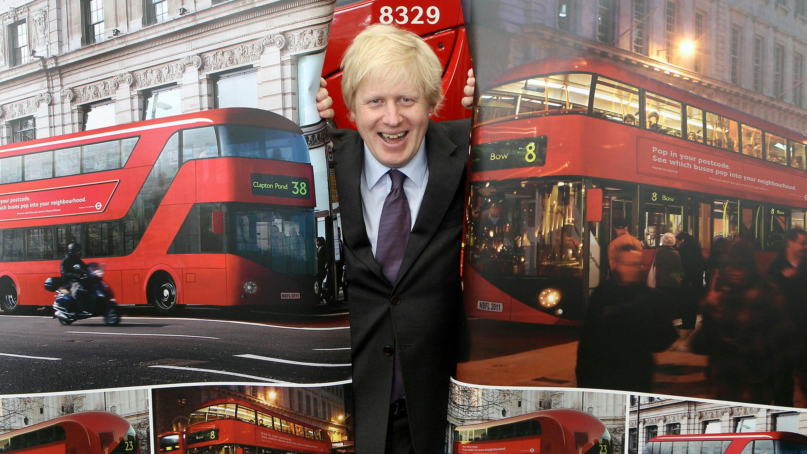 Wir sehen Boris Johnson, der hinter einem Vorhang steht, der voll mit roten Bussen ist – und durch eine Öffnung im Vorhang lugt. 