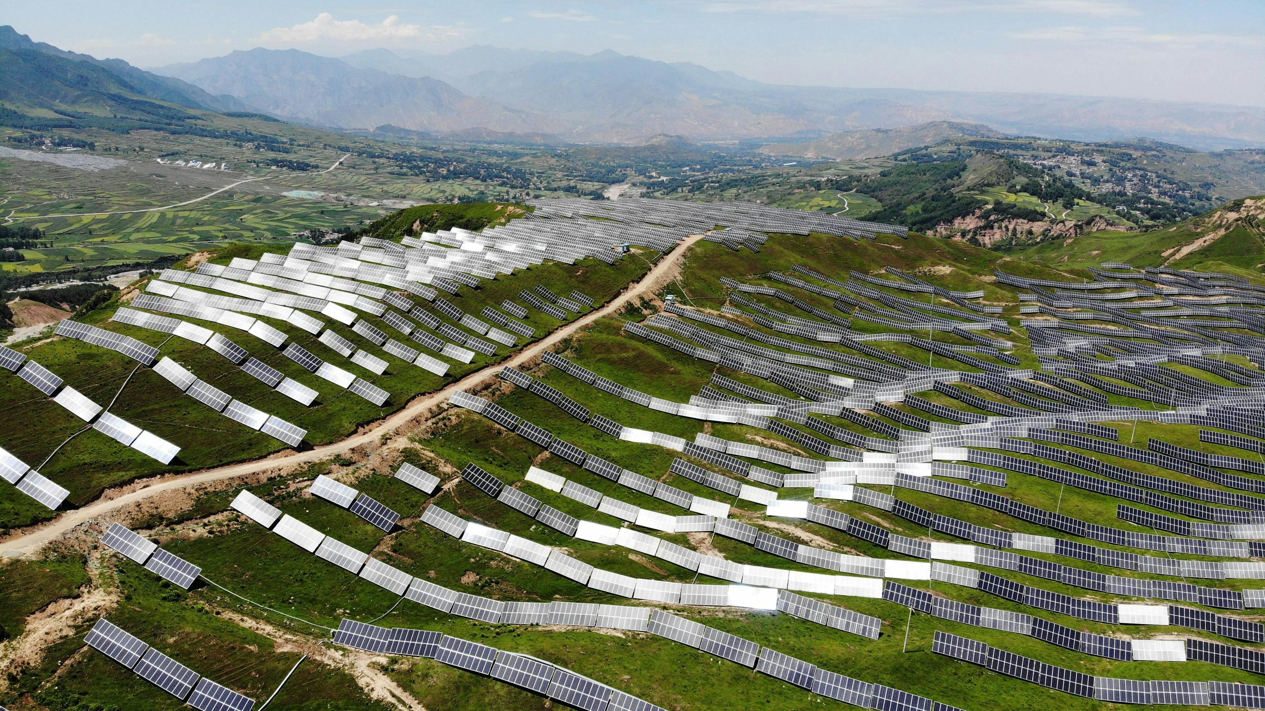 Wir sehen eine Luftaufnahme von Sonnenkollektoren in einem Ergänzungskraftwerk, das Landwirtschaft und Photovoltaik im Landkreis Jishishan, Provinz Gansu, China, kombiniert.