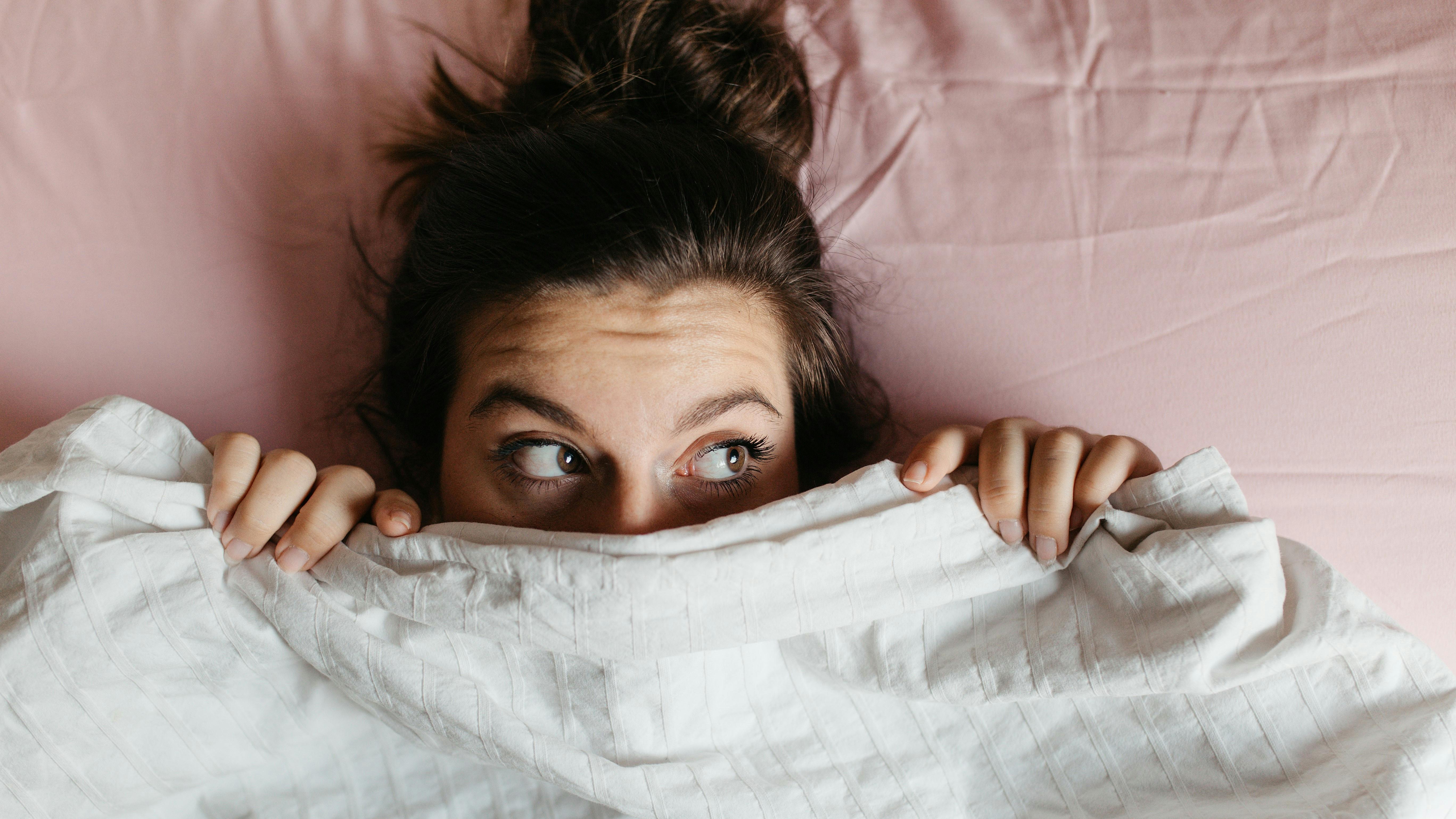 Eine Frau lugt unter der Bettdecke hervor.