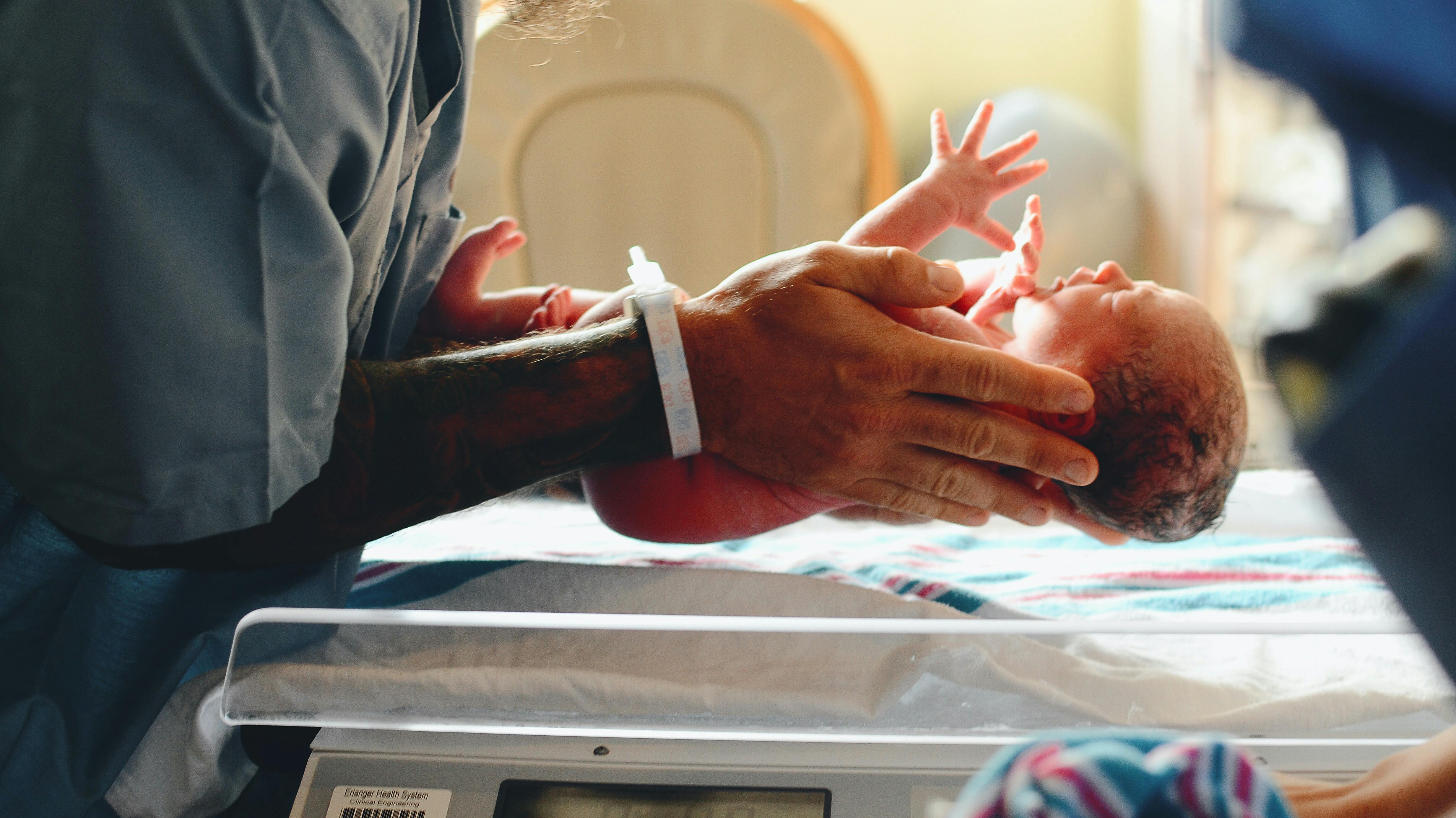 Eine Person hält einen Säugling über eine Neugeborenen Waage
