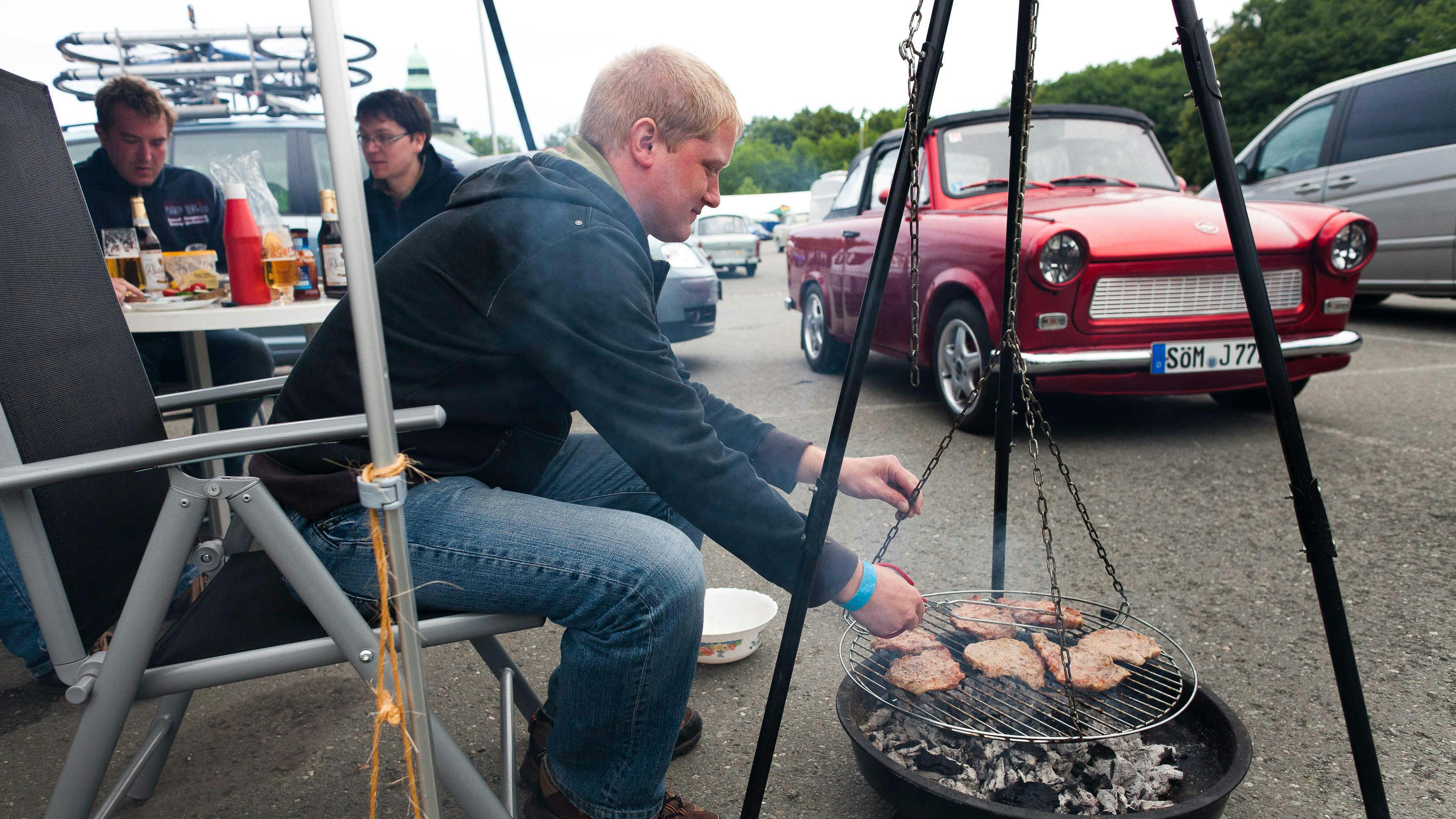 Ein Mann grillt vor seinem Trabant, während sich Fans und Besitzer von Trabants aus der DDR-Zeit versammeln .