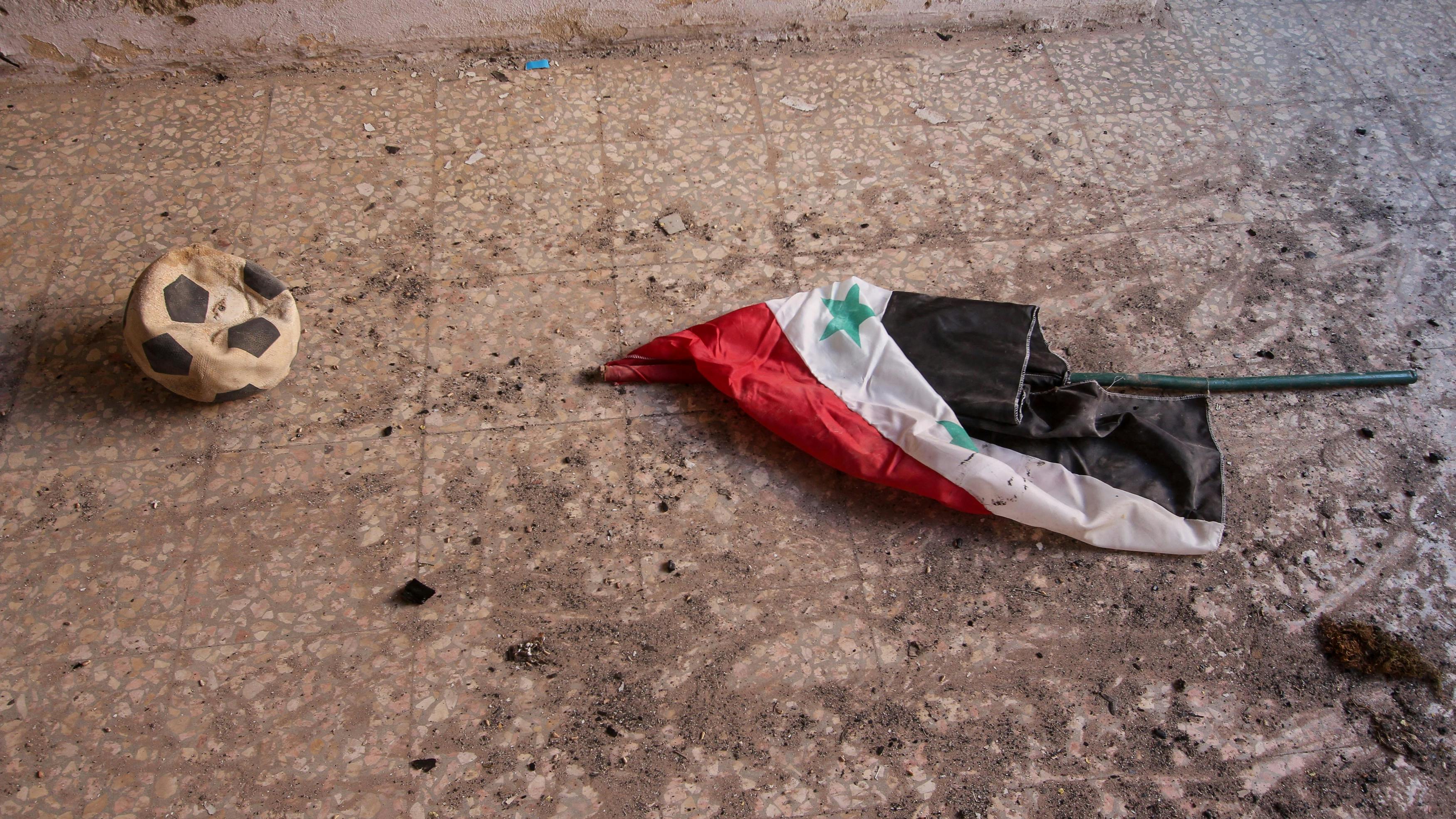 Eine syrische Flagge lieg im Dreck auf dem Boden. 