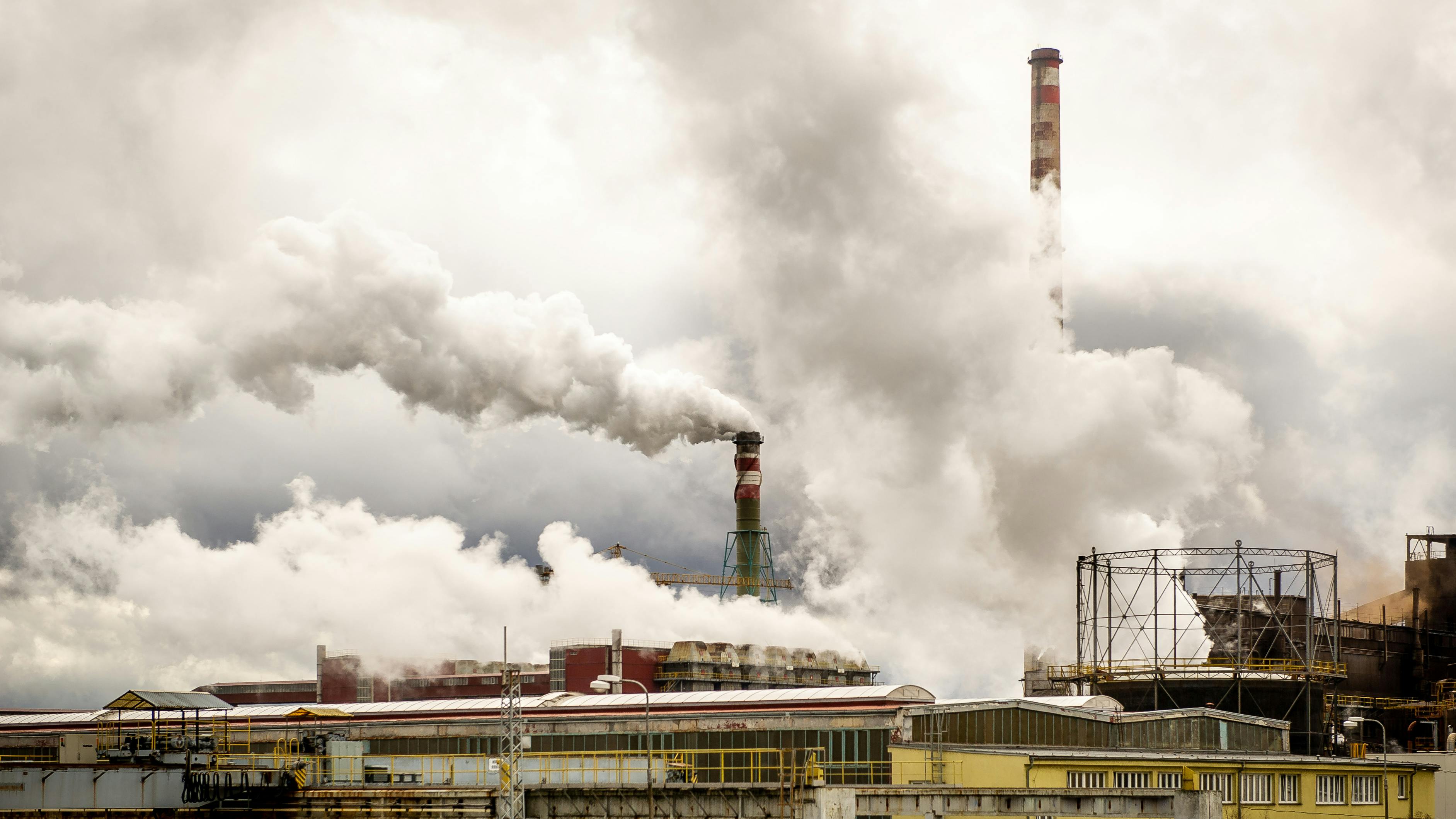 Raucheschwaden steigen aus großen Industrieschornsteinen einer Fabrik auf.