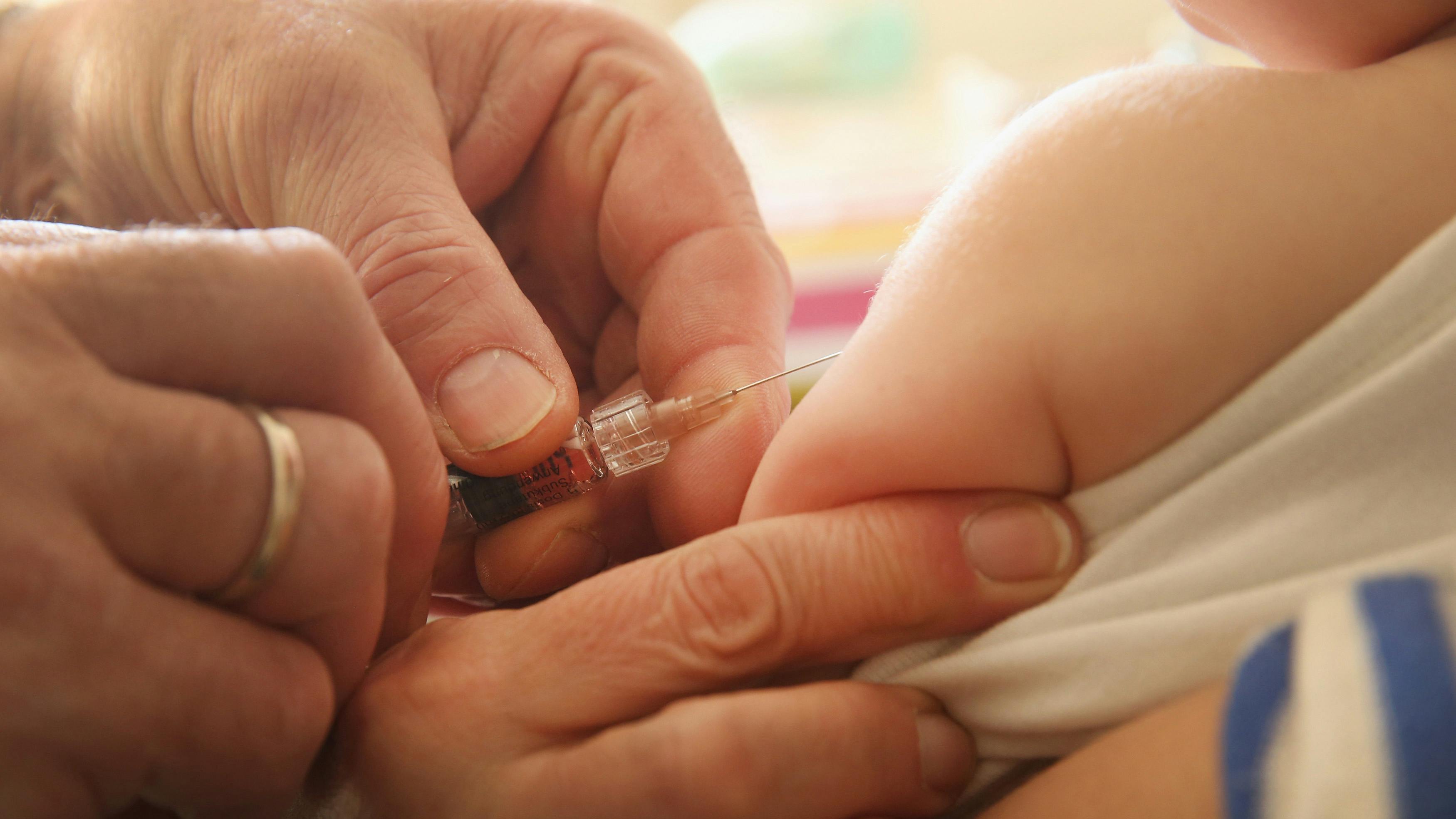 Nahaufnahme einer Hand, mit einer Spritze gut sichtbar, die ein Kleinkind impft.