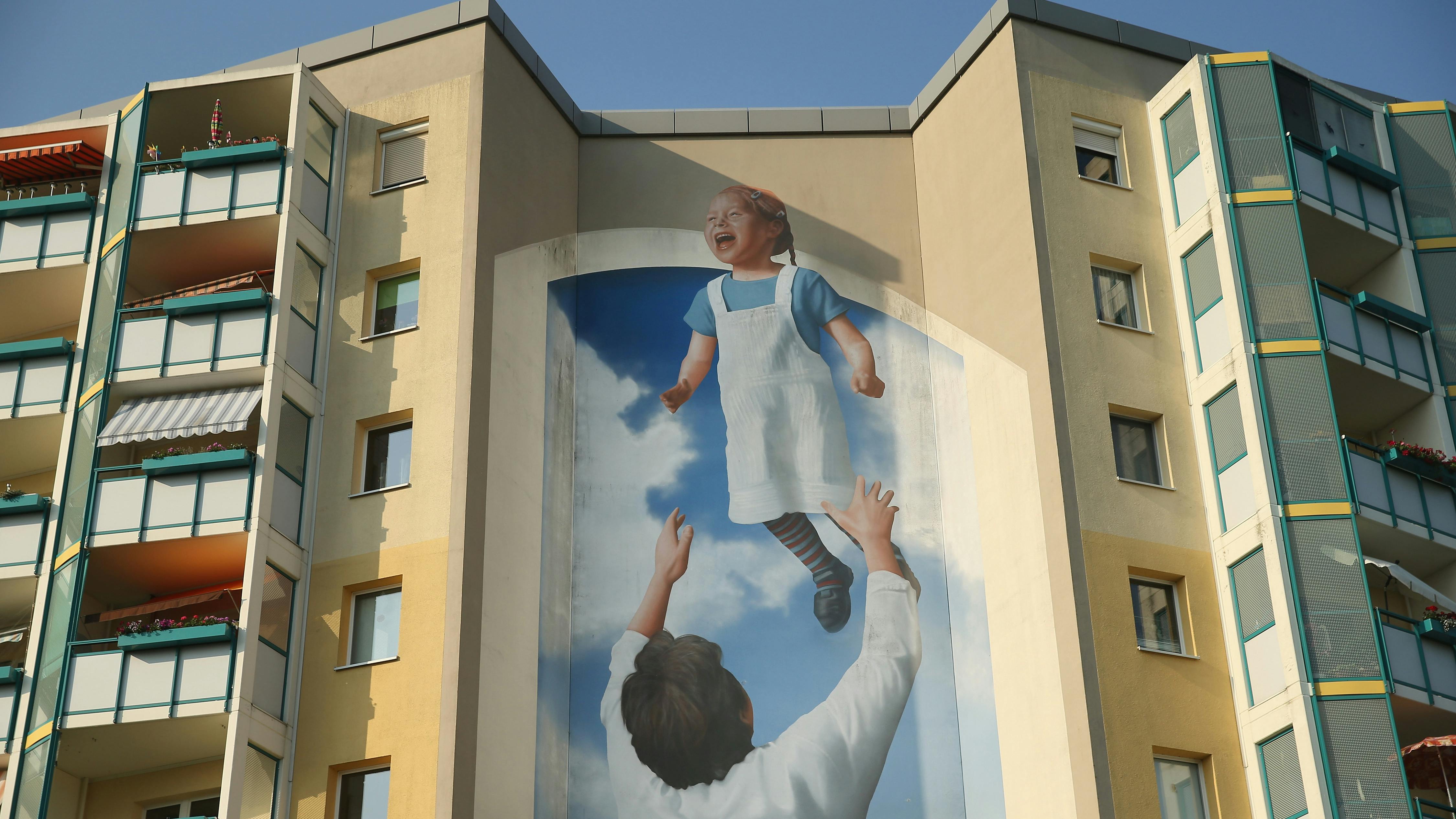 Ein Wandmalerei an der Seite eines kommunistischen Wohnblocks zeigt einen Vater, der seine Tochter in die Luft wirft.
