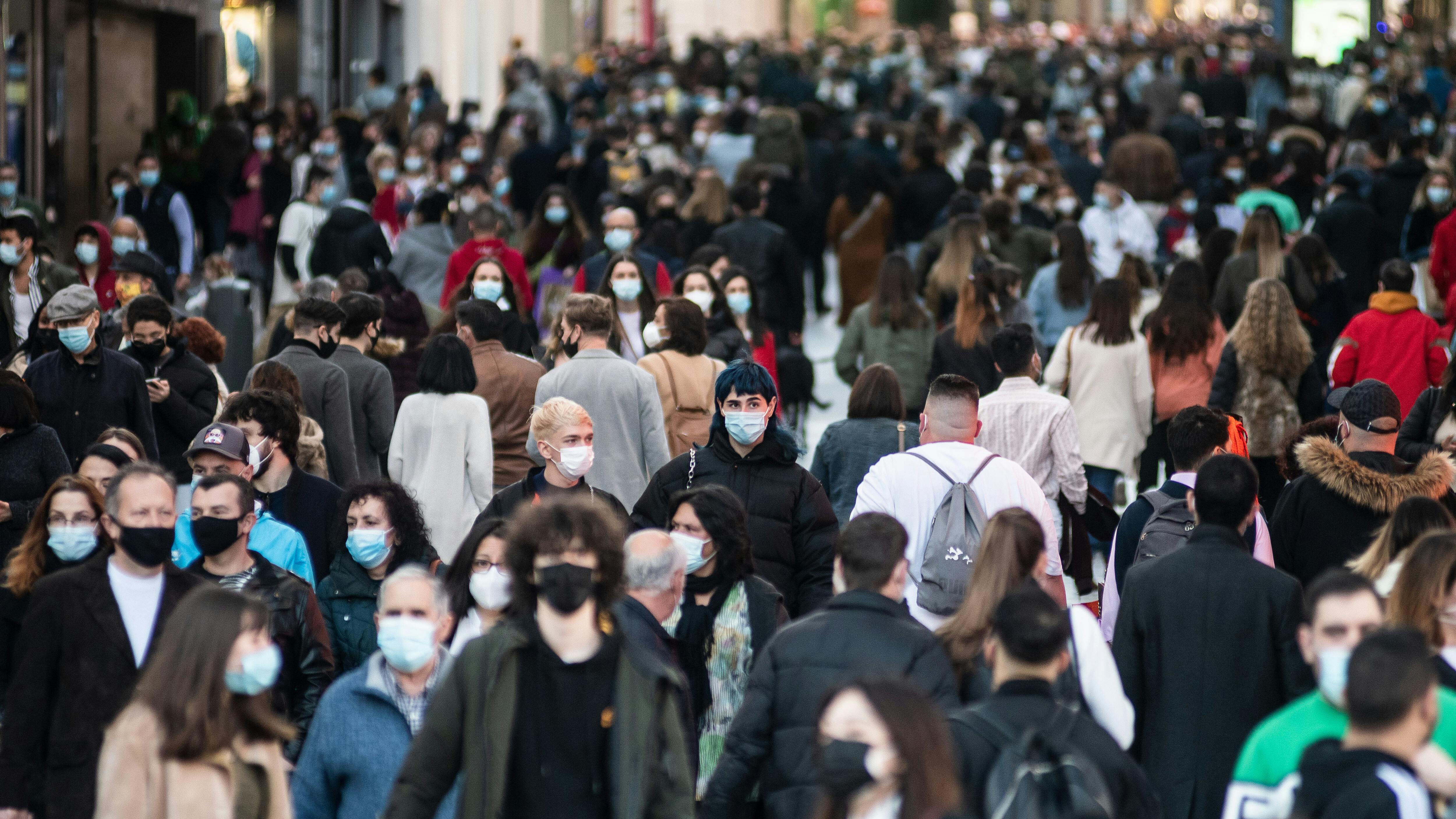 Menschenmengen mit Gesichtsmasken, um die Ausbreitung des Coronavirus zu stoppen, laufen durch die Innenstadt.