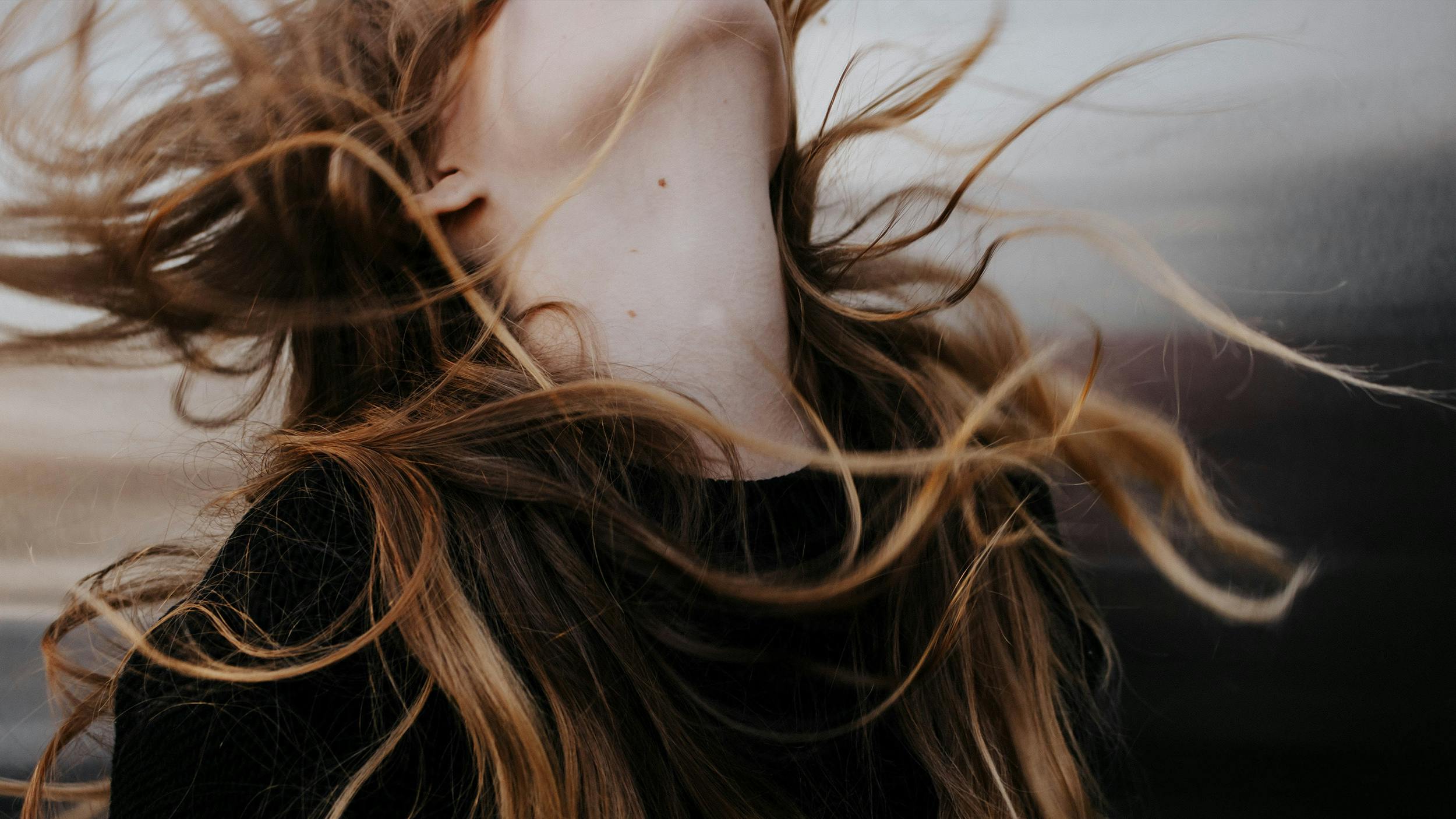 Man sieht den Hals und die wilden Haare einer Frau, vom Wind zerzaust, kein Gesicht