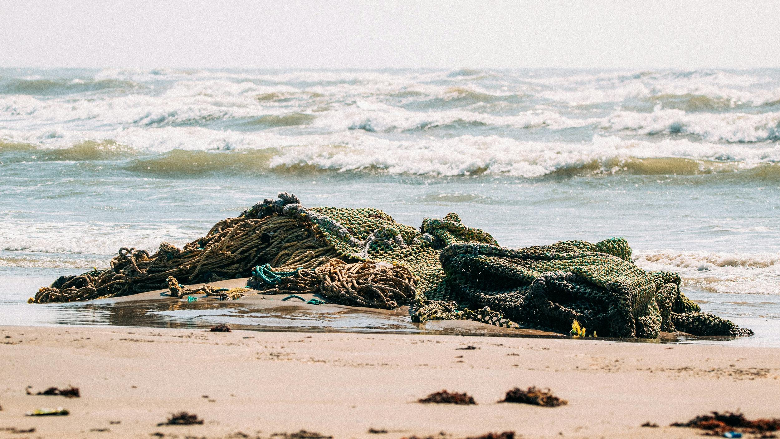 Ein altes Fischnetz liegt liegt am Strand, im Hintergrund ist das Meer zu sehen.