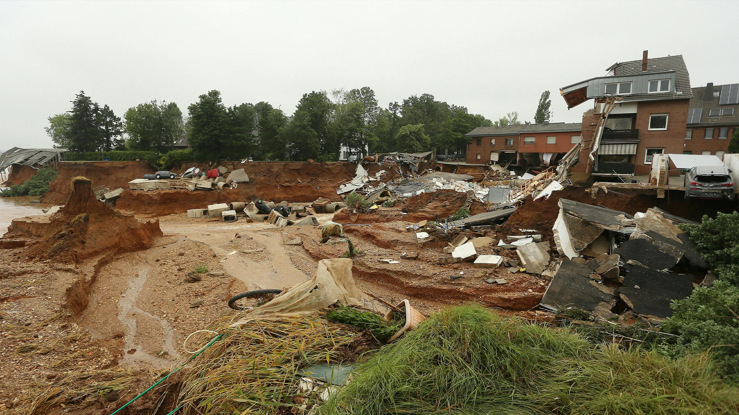 Eine Szene aus dem Ahrtal von vor einem Jahr. Durch die Flut gab es einen Erdrutsch, rechts im Bild sieht man die Trümmer eines betroffenen Hauses. In der Ferne sieht man mehrere Autos, die abgerutscht sind. 