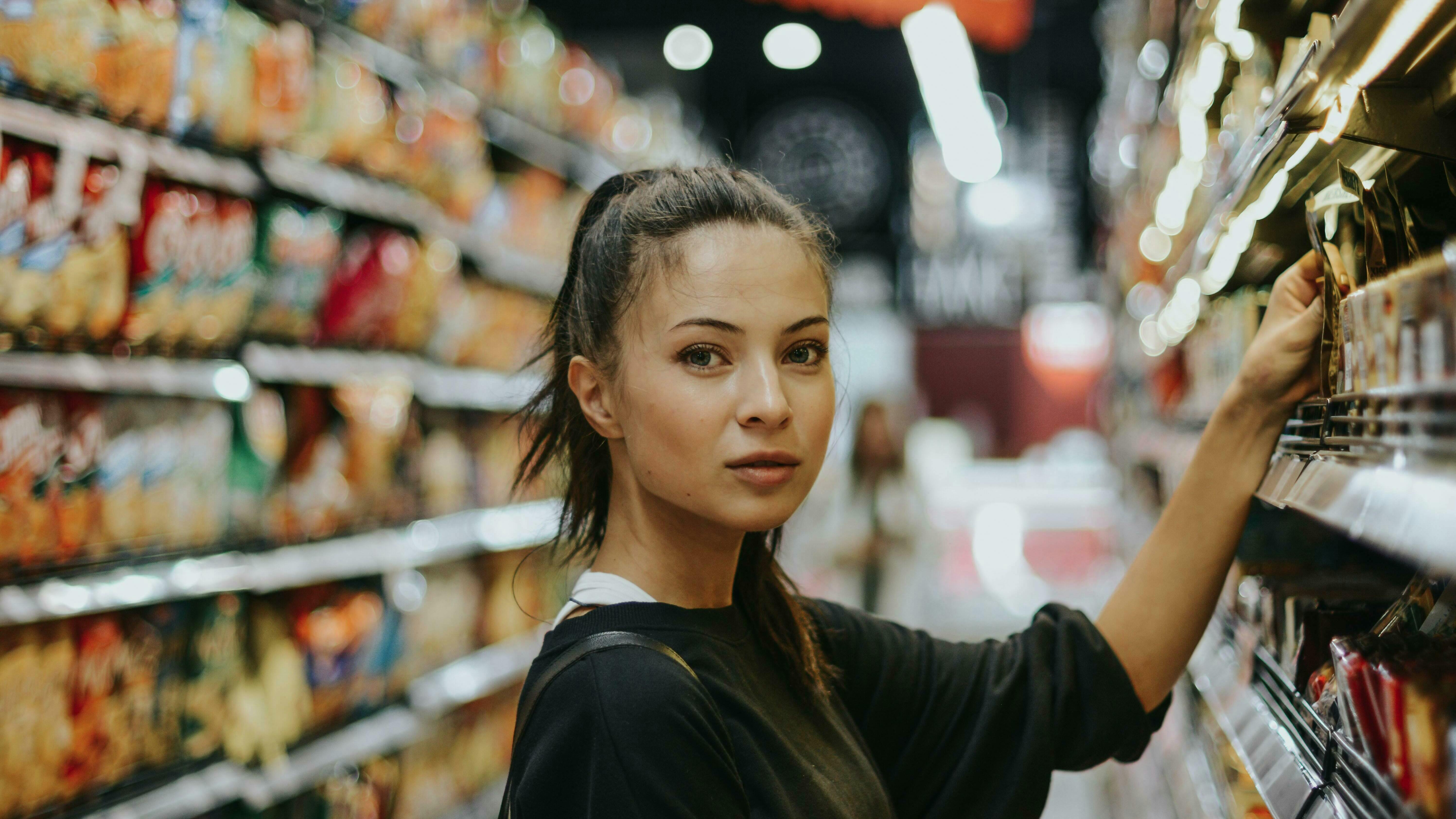 Eine Frau steht in einem Supermarkt und greift etwas aus dem Regal.