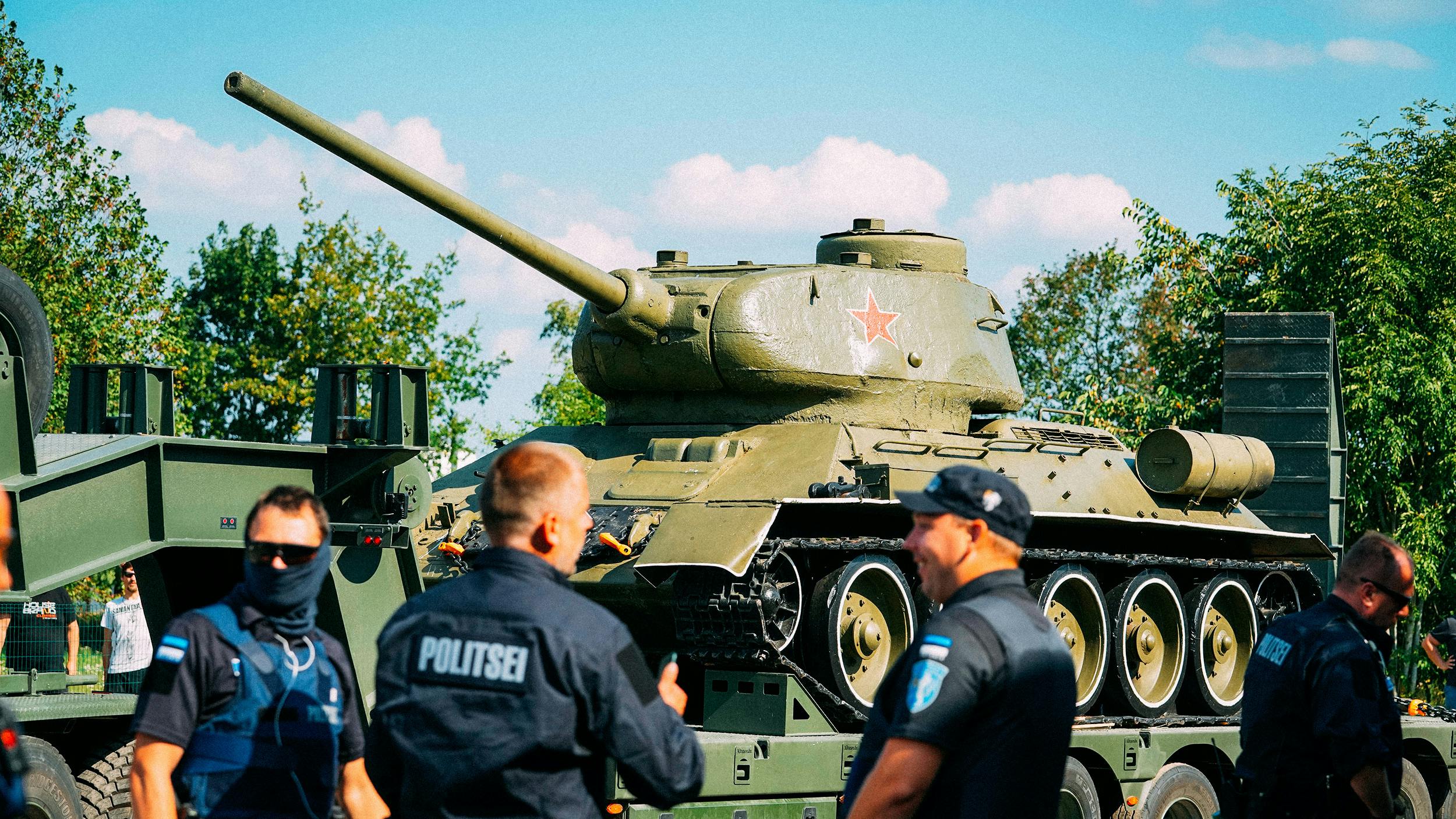 Man sieht einen Panzer aus dem 2. Weltkrieg, der abtransportiert wird, davor 4 estnische Polizisten, der eine mit Sonnenbrille und Sturmmaske, auf dem Panzer prangt ein roter Stern, Symbol der Sowjets.