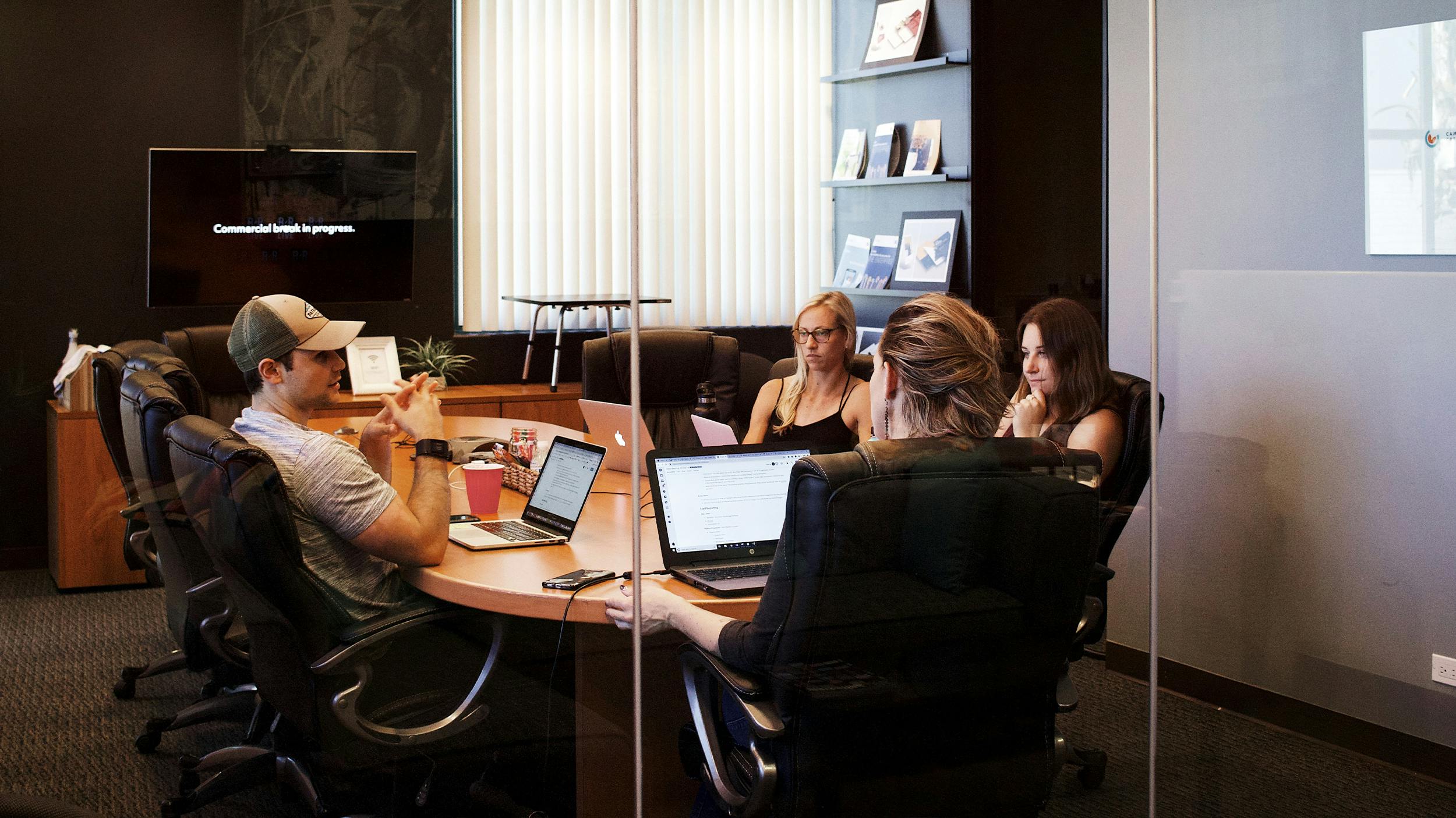 Vier Menschen sitzen um einen Tisch herum. Vor ihnen stehen Laptops.