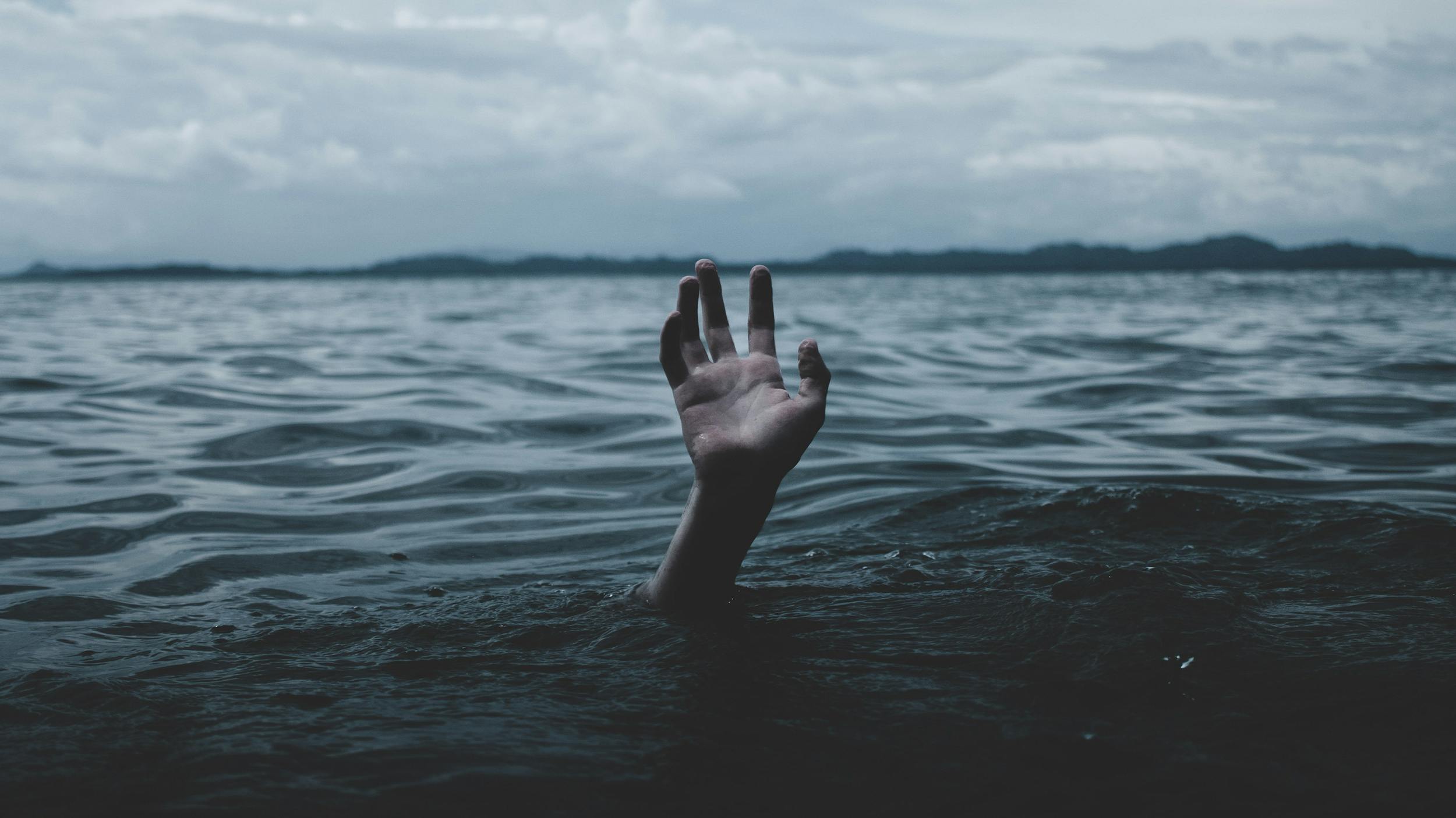 Eine Hand einer ertrinkenden Person erstreckt sich aus dem Meer. 