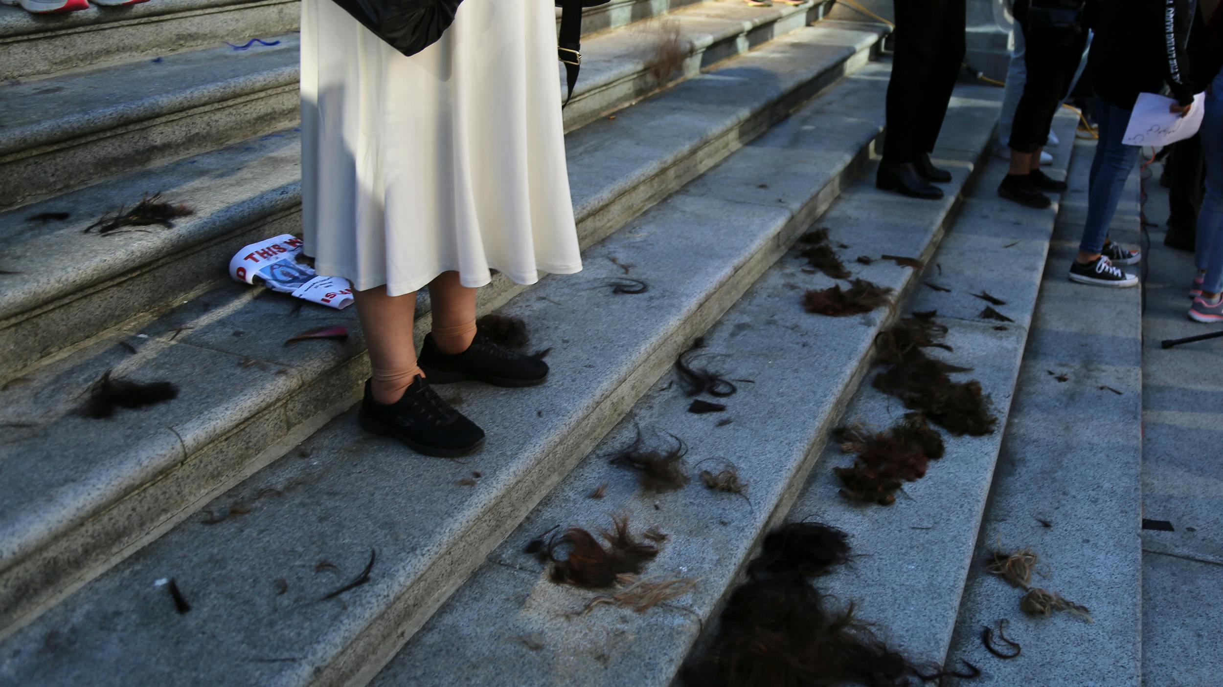 Abgeschnittene Haare auf einer Treppe. Ein Mensch steht auf den Stufen, man erkennt nur seine Beine.