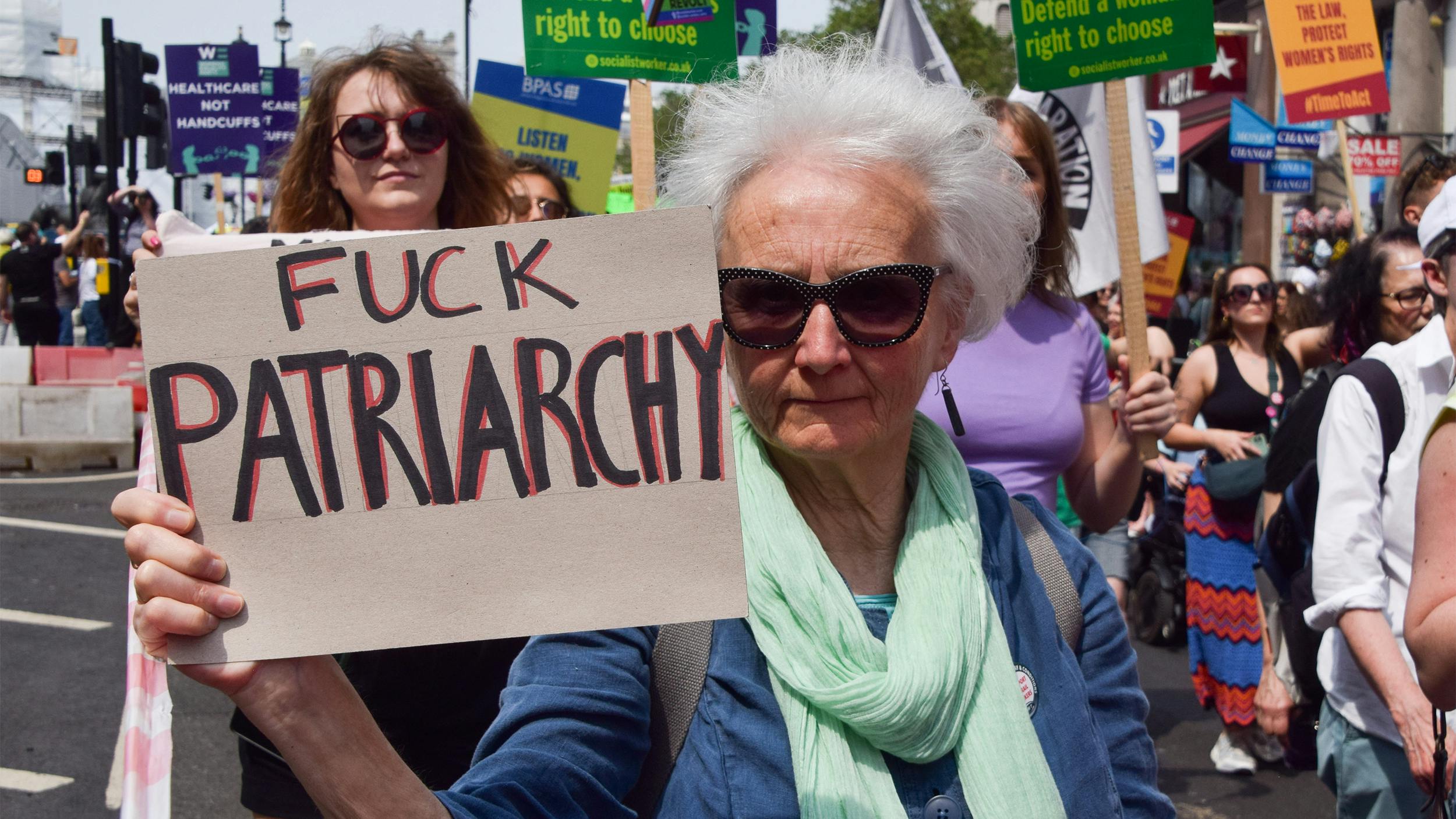 Eine ältere Frau mit weißem Haar hält auf einer Demo ein Plakat in der Hand, auf dem steht: Fuck Patriarchy