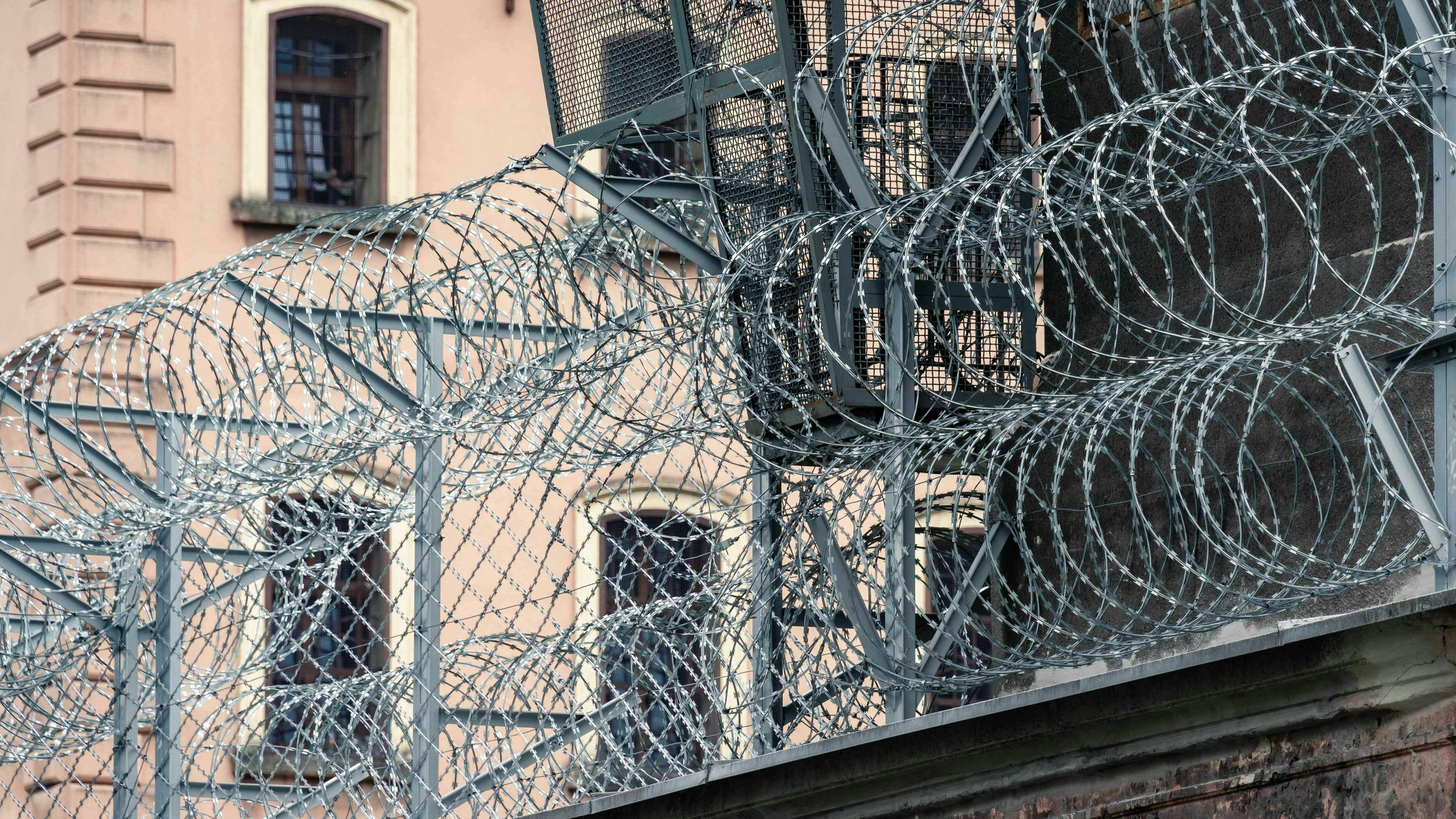 Außenaufnahme eines Gefängnisses. Auf einer Mauer liegt Stacheldraht.