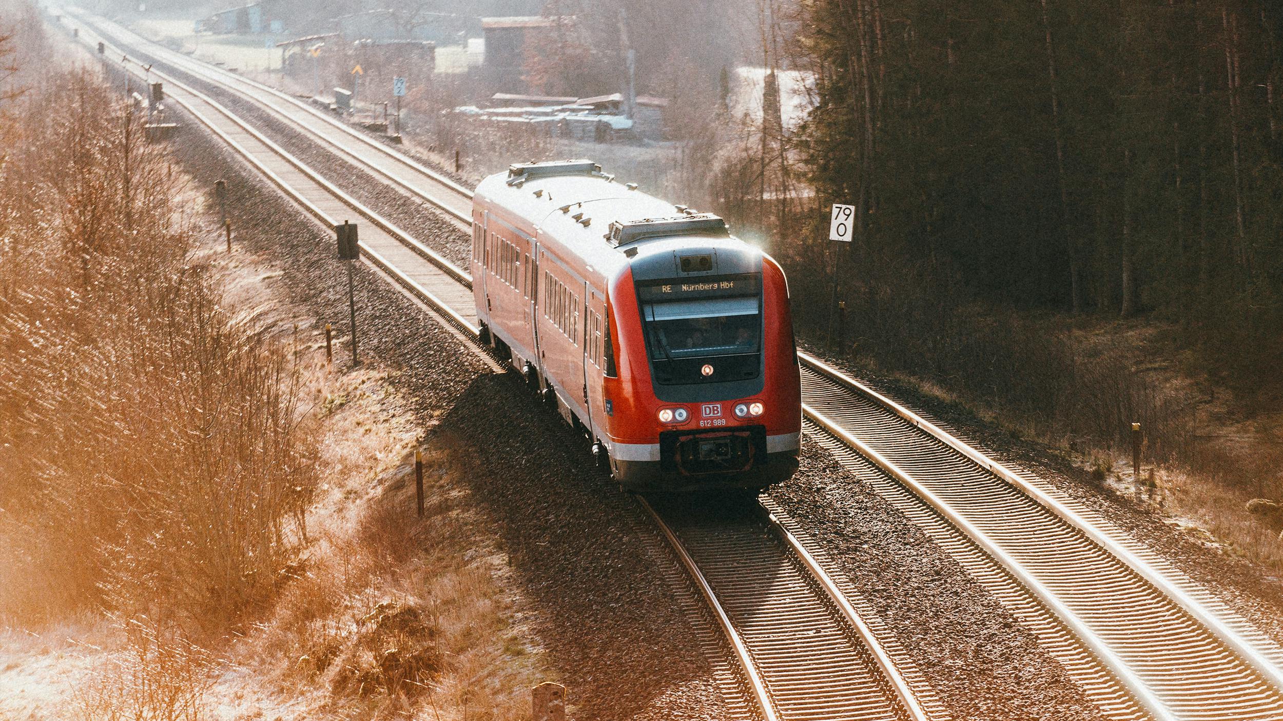 Man sieht einen kurzen Regionalzug der Deutschen Bahn von etwas weiter weg durch eine herbstliche Landschaft fahren.