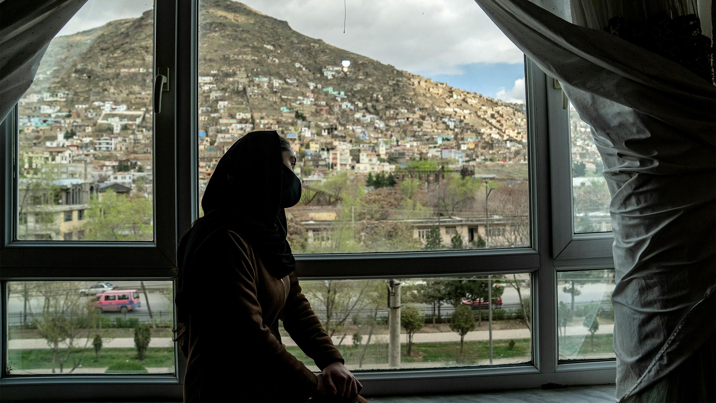 Eine junge verschleierte Frau sitzt am Fenster und blickt hinaus.