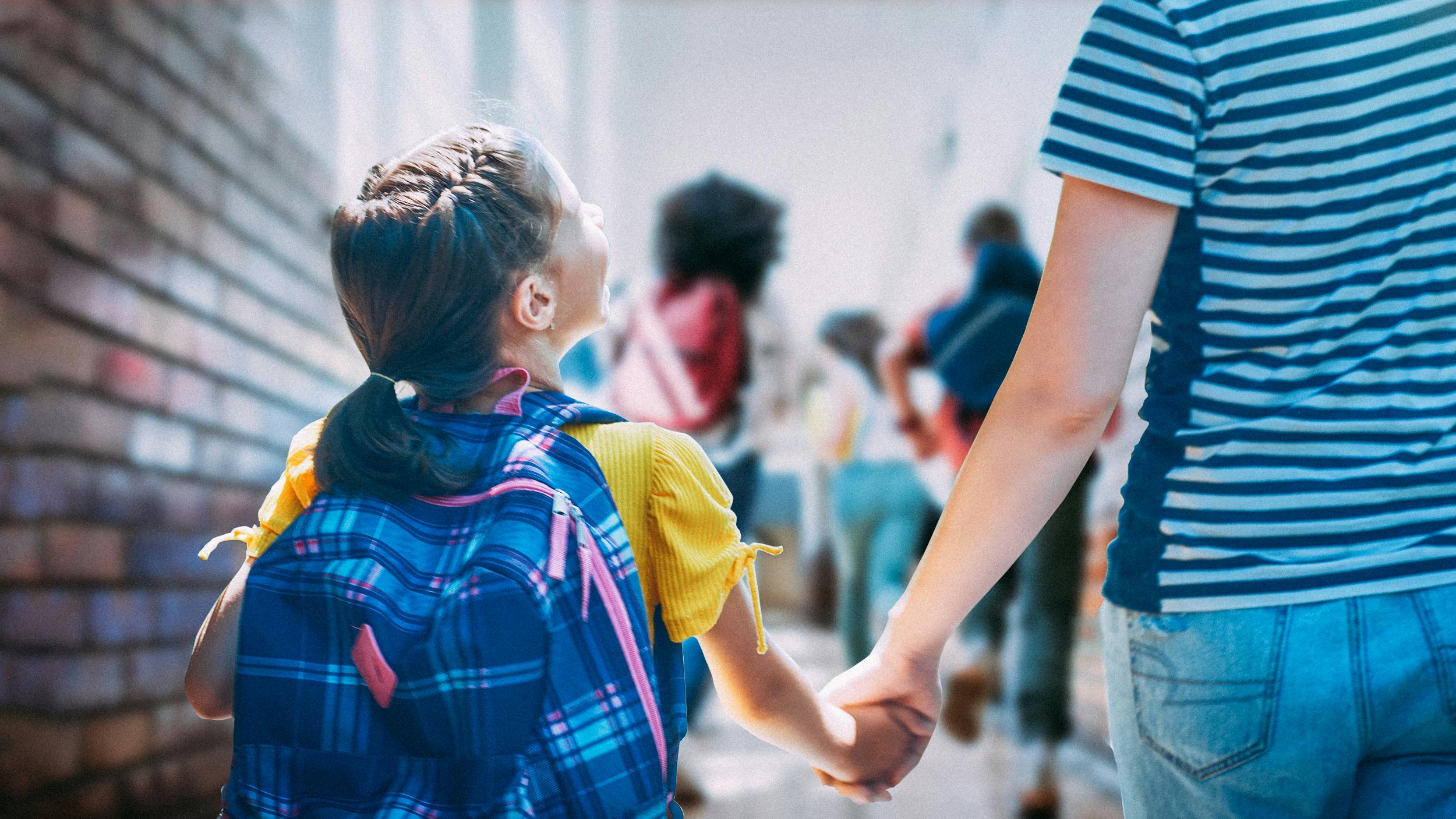 Ein Schulkind geht an der Hand einer Frau einen Gang im Schulgebäude entlang.