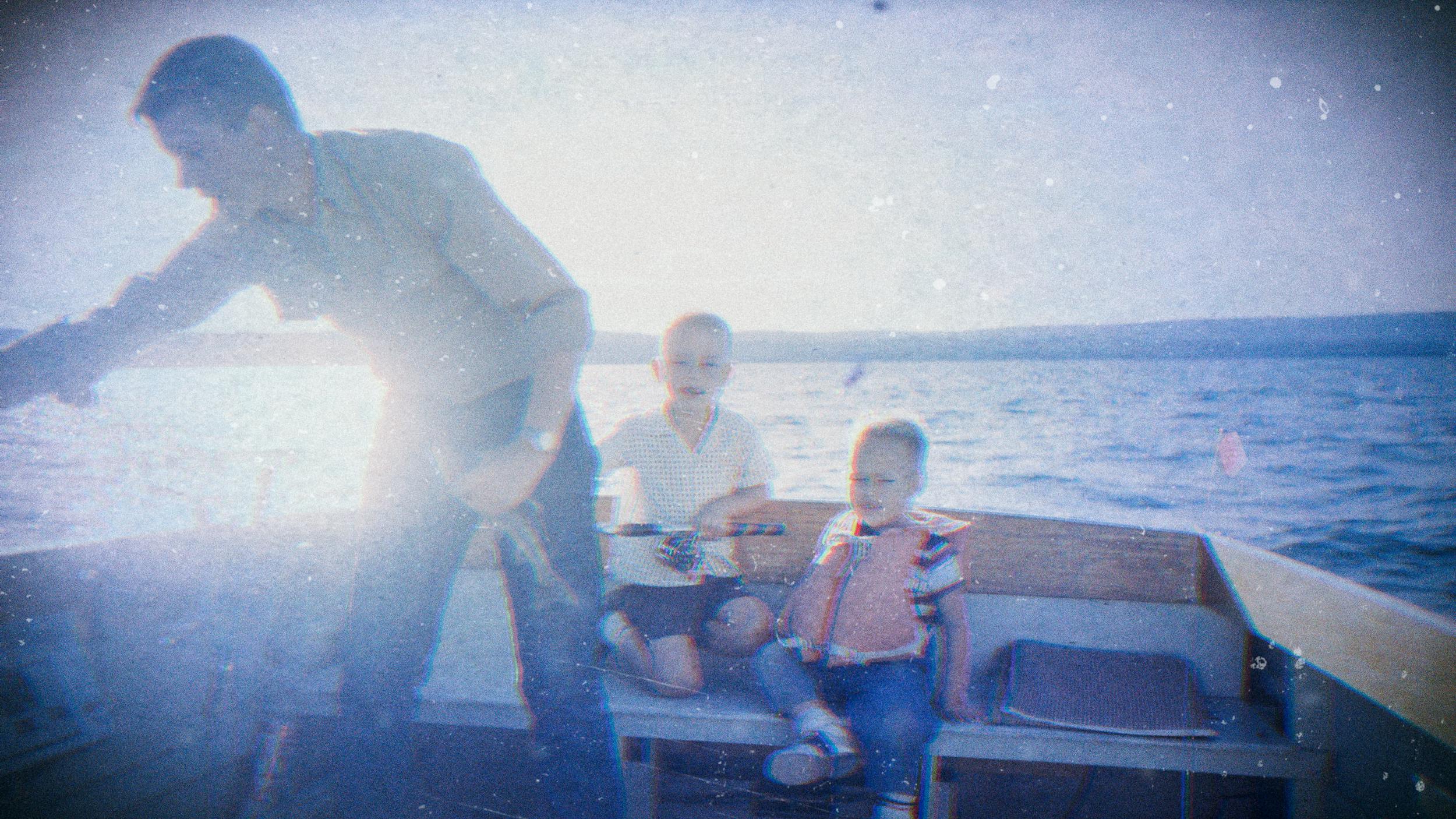 Ein altes Familienfoto von einem Vater mit seinen beiden Kindern. Sie befinden sich auf einem Boot und angeln.