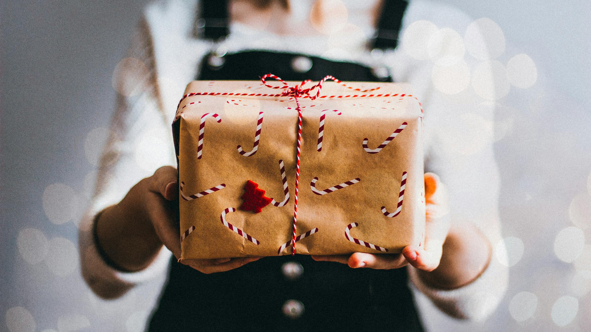 Eine Frau hält ein Weihnachtsgeschenk in die Kamera, es ist mit Zuckerstangen verziert. 