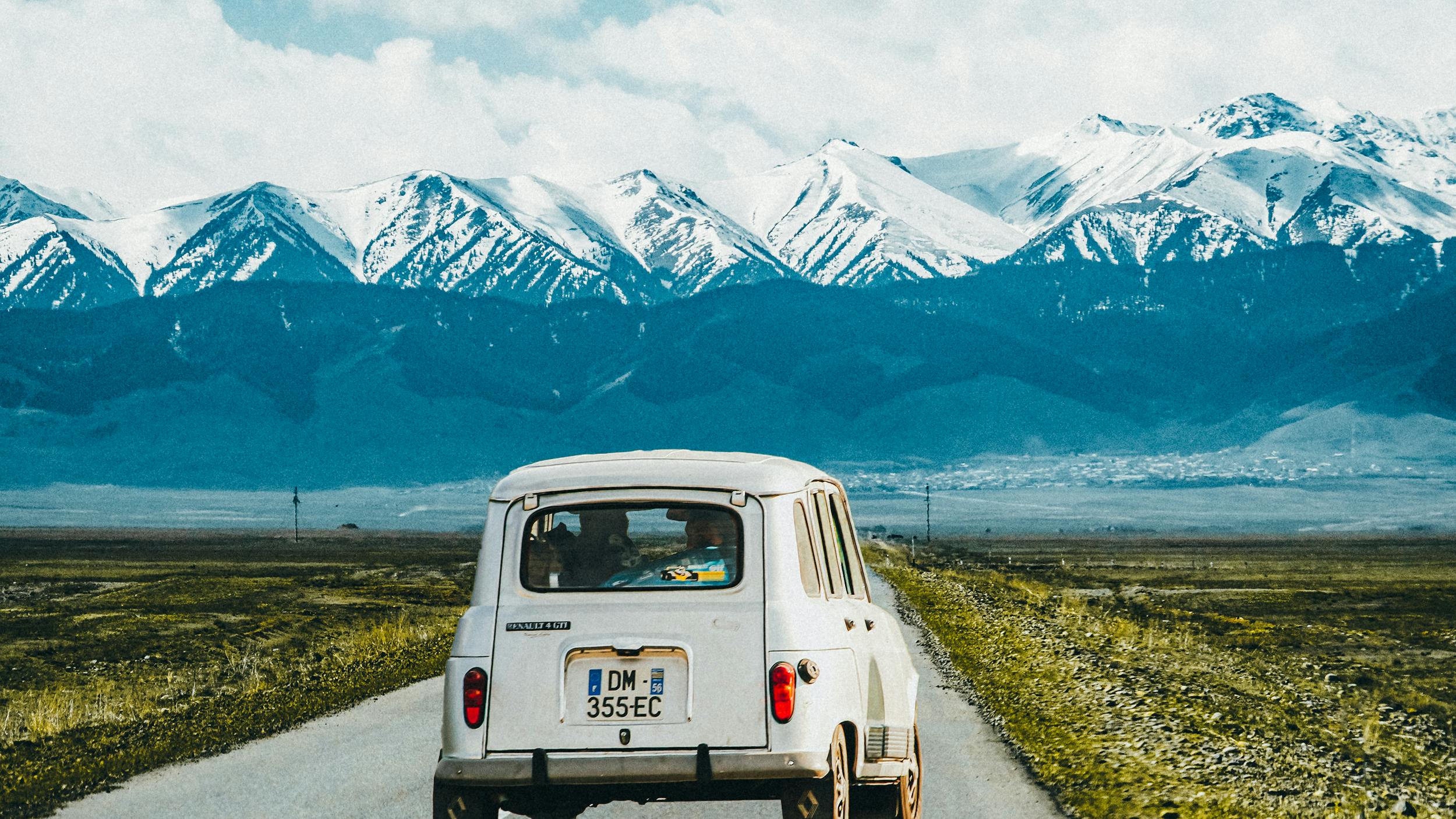 Ein Auto fährt auf einer kasachischen Landstraße. Im Hintergrund sind Berge zu sehen.