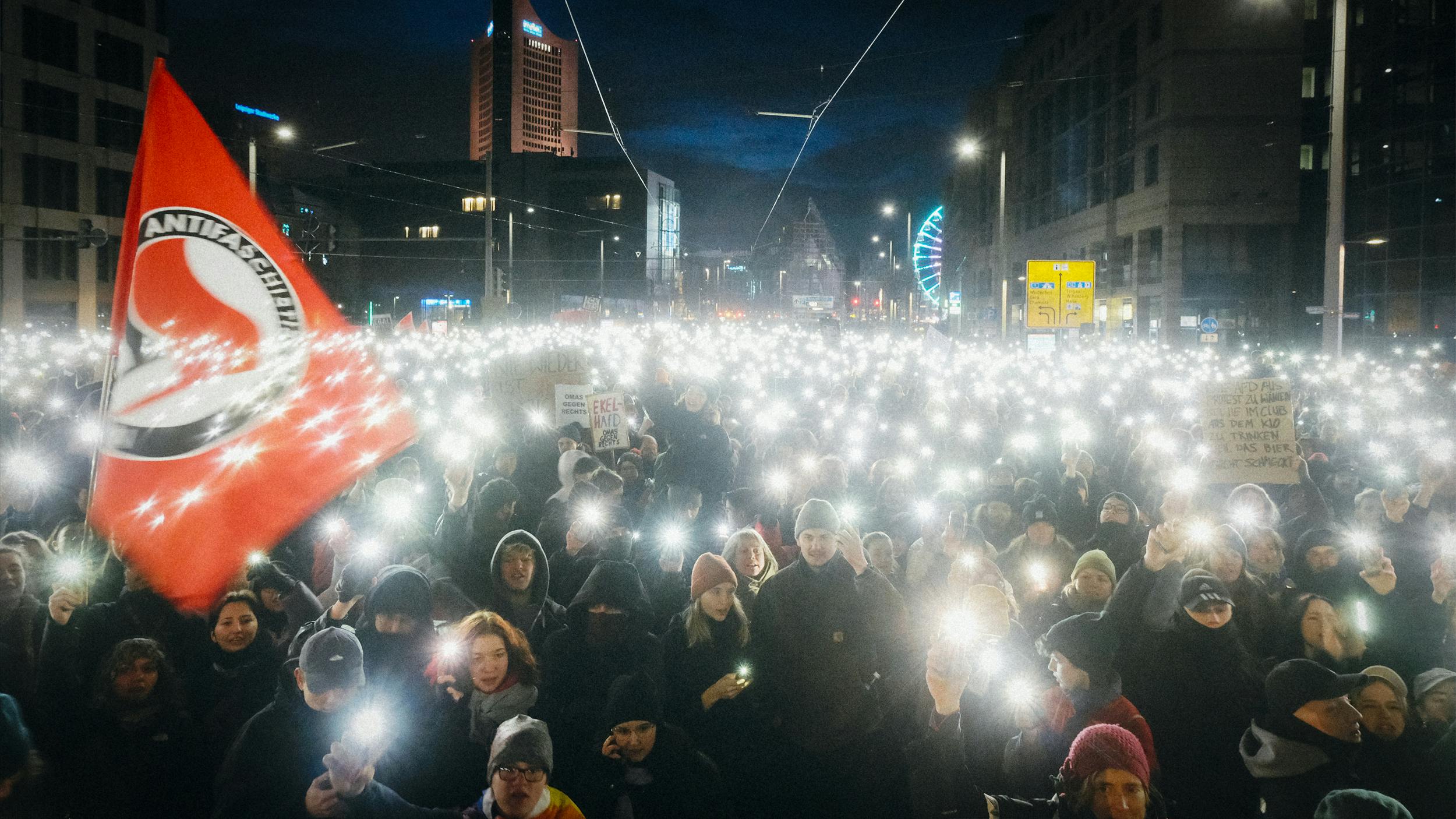 Viele Menschen stehen auf einem öffentlichen Platz, um gegen die AfD zu demonstrieren. Es ist dunkel, sie halten die Taschenlampen ihrer Handys in die Höhe.