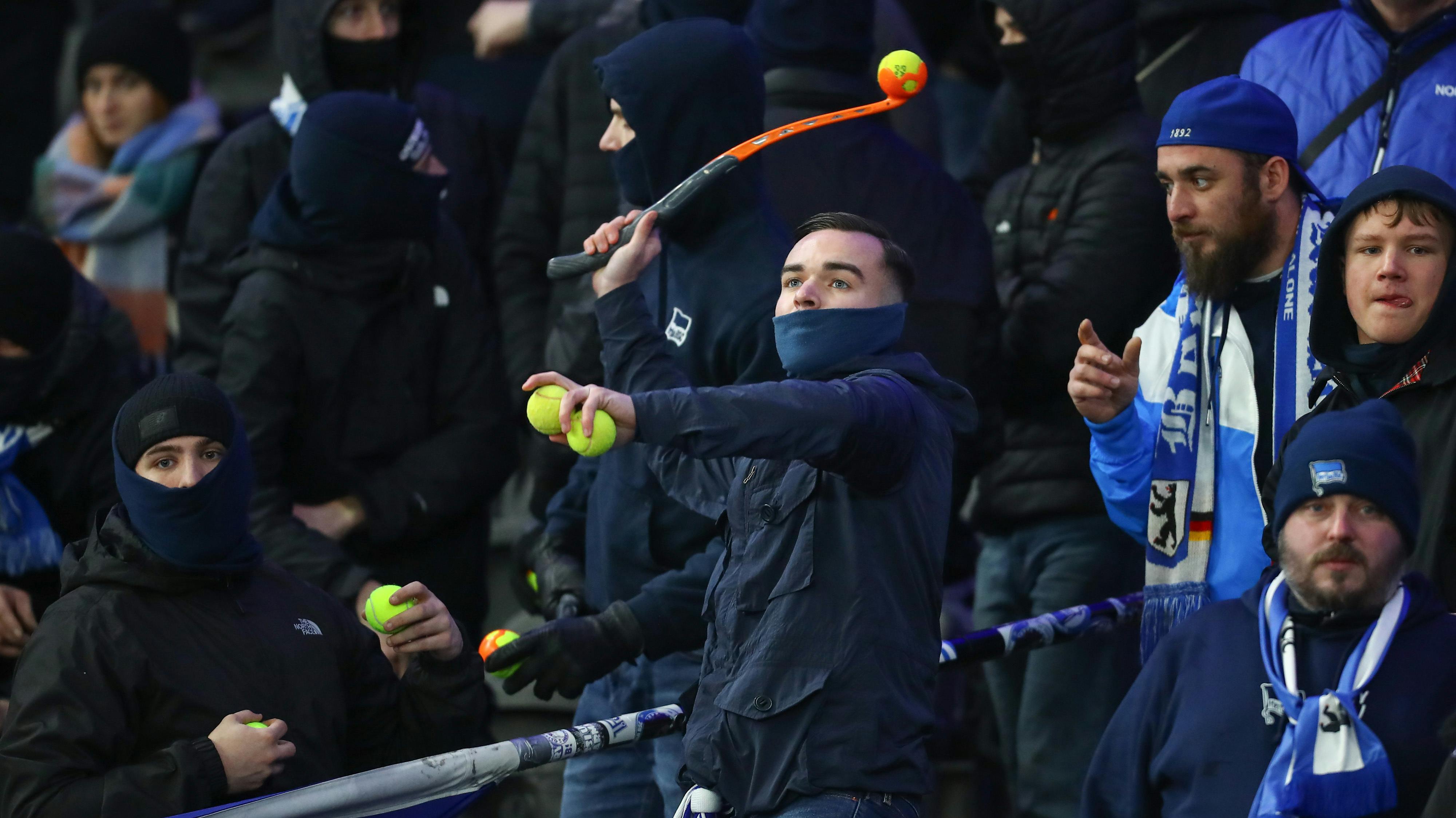 Fußballfans stehen auf einer Tribüne und werdeN Tennisbälle auf das Spielfeld