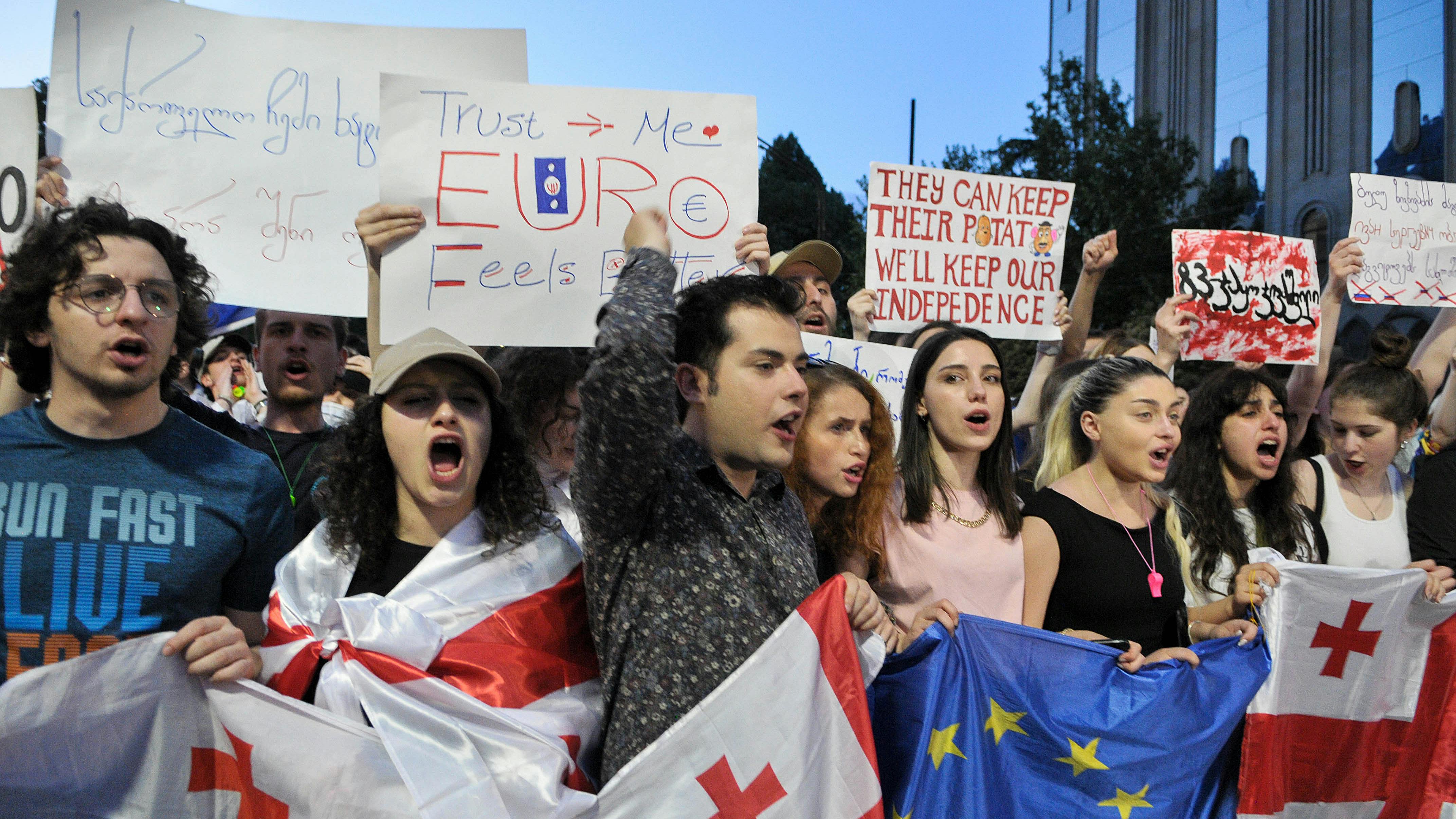 Mehrere Personen halten Schilder in die Höhe und tragen EU- und georgische Flaggen um die Schultern.