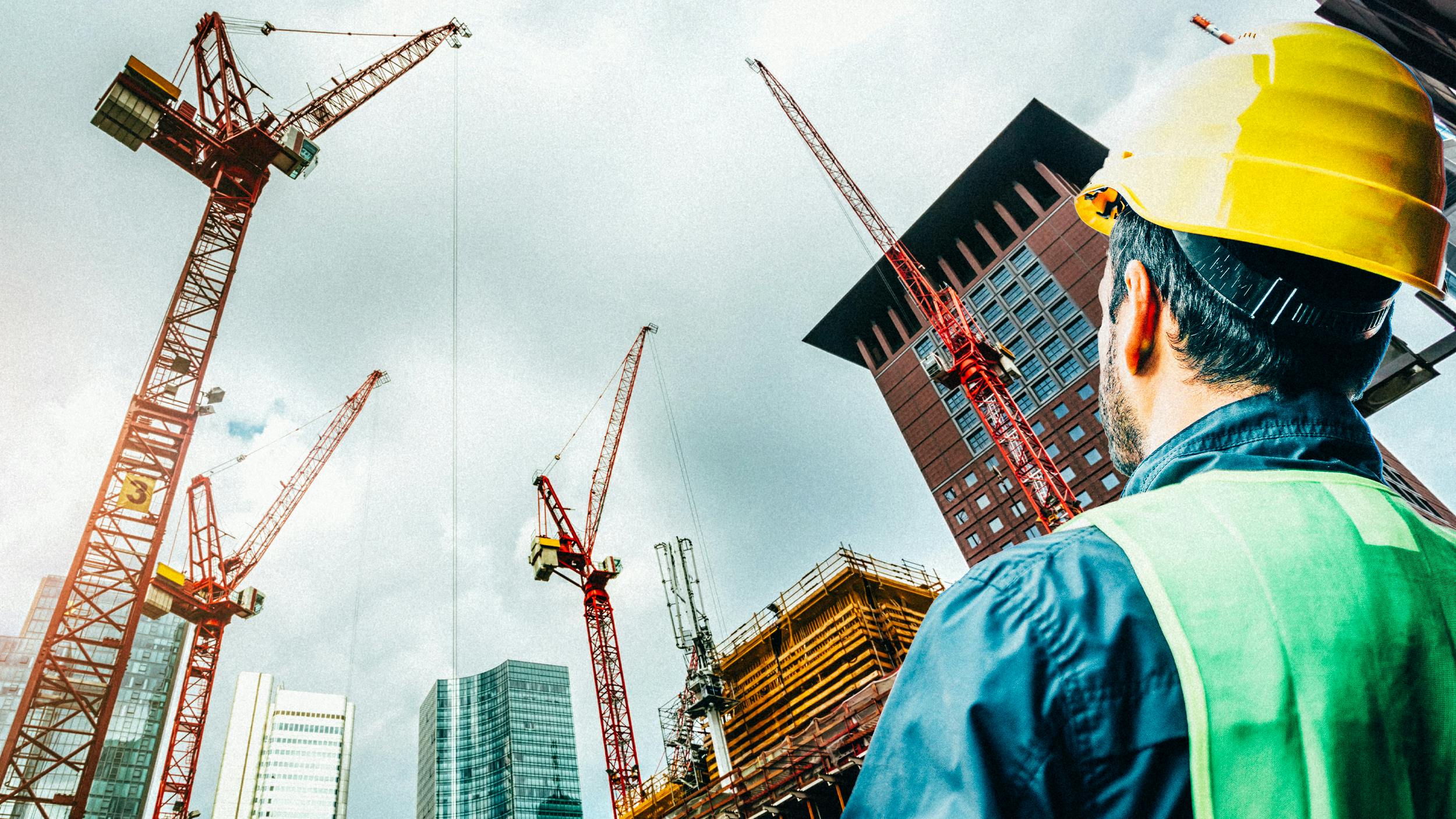 Ein Mann mit Helm blickt auf eine Baustelle. Viele Baukräne erreichten Hochhäuser.