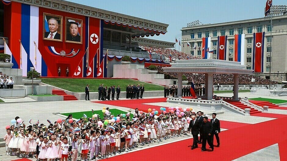 Wladimir Putin und Kim Jong-un spazieren auf einem großen Platz vor einer Menschenmenge mit vielen Fahnen.