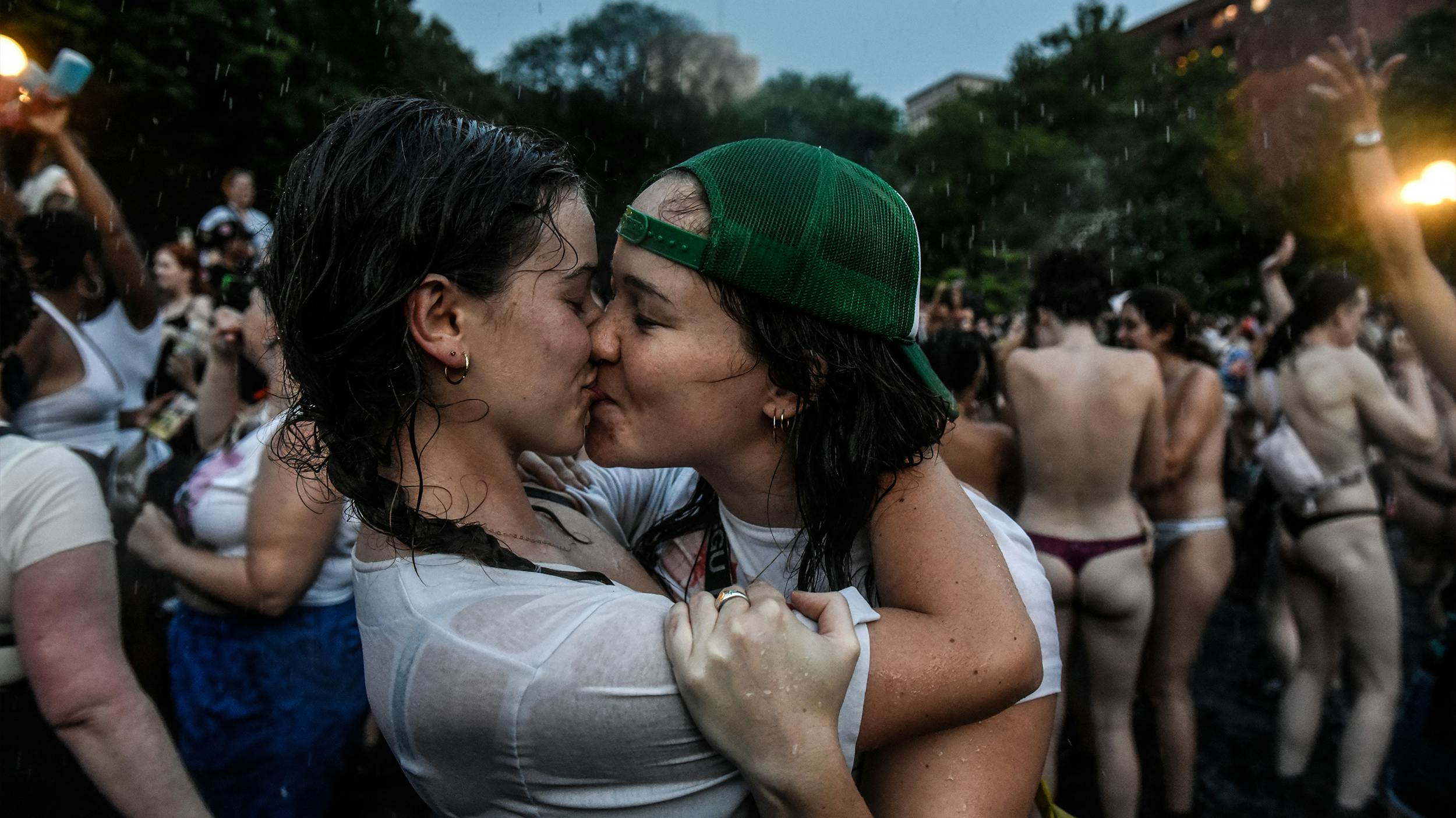 Zwei Frauen küssen sich, im Hintergrund sind viele weitere Menschen zu sehen.