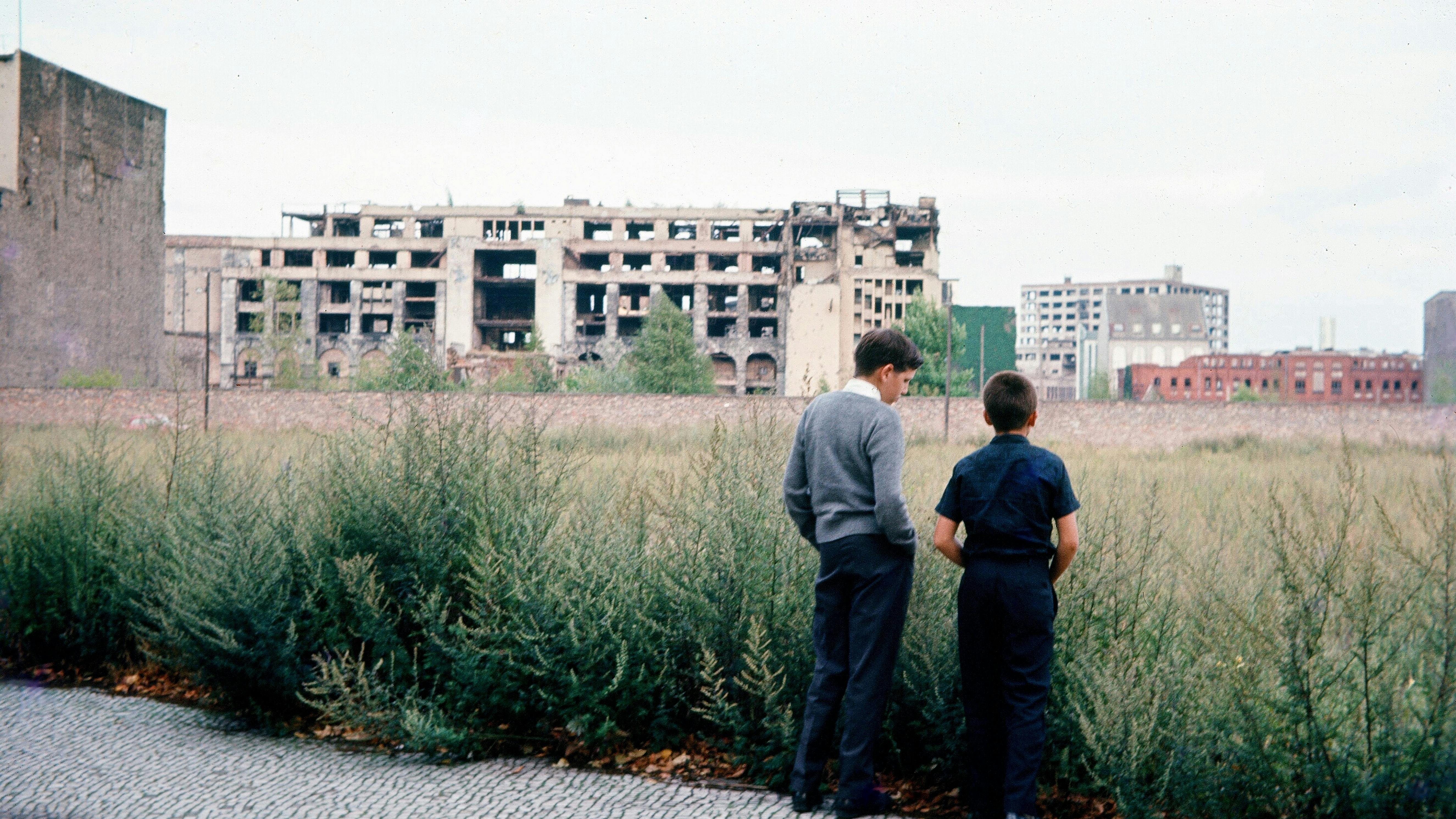 Zwei Jungen stehen vor einem Feld und blicken auf eine Hausruine