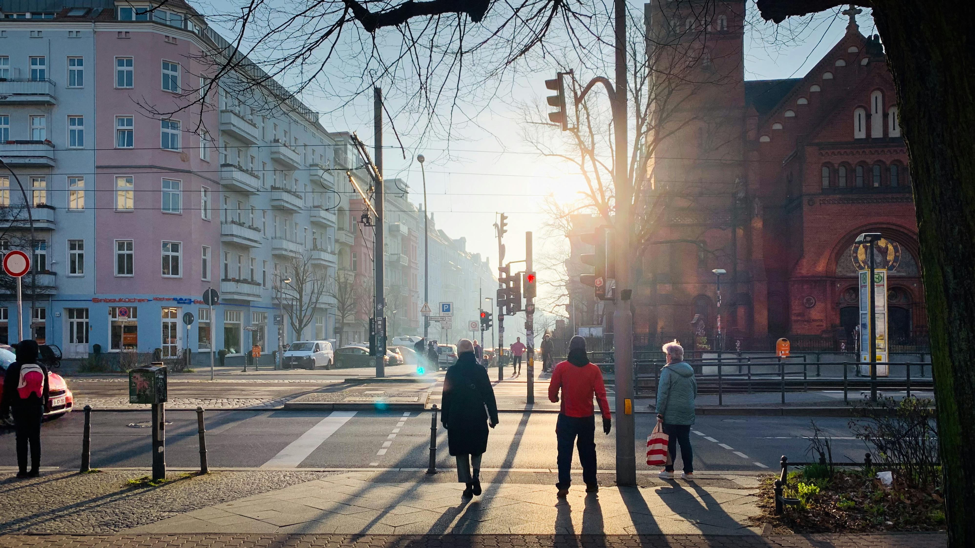 Eine Fußgängerampel im Morgenlicht. Leute überqueren die Straße.