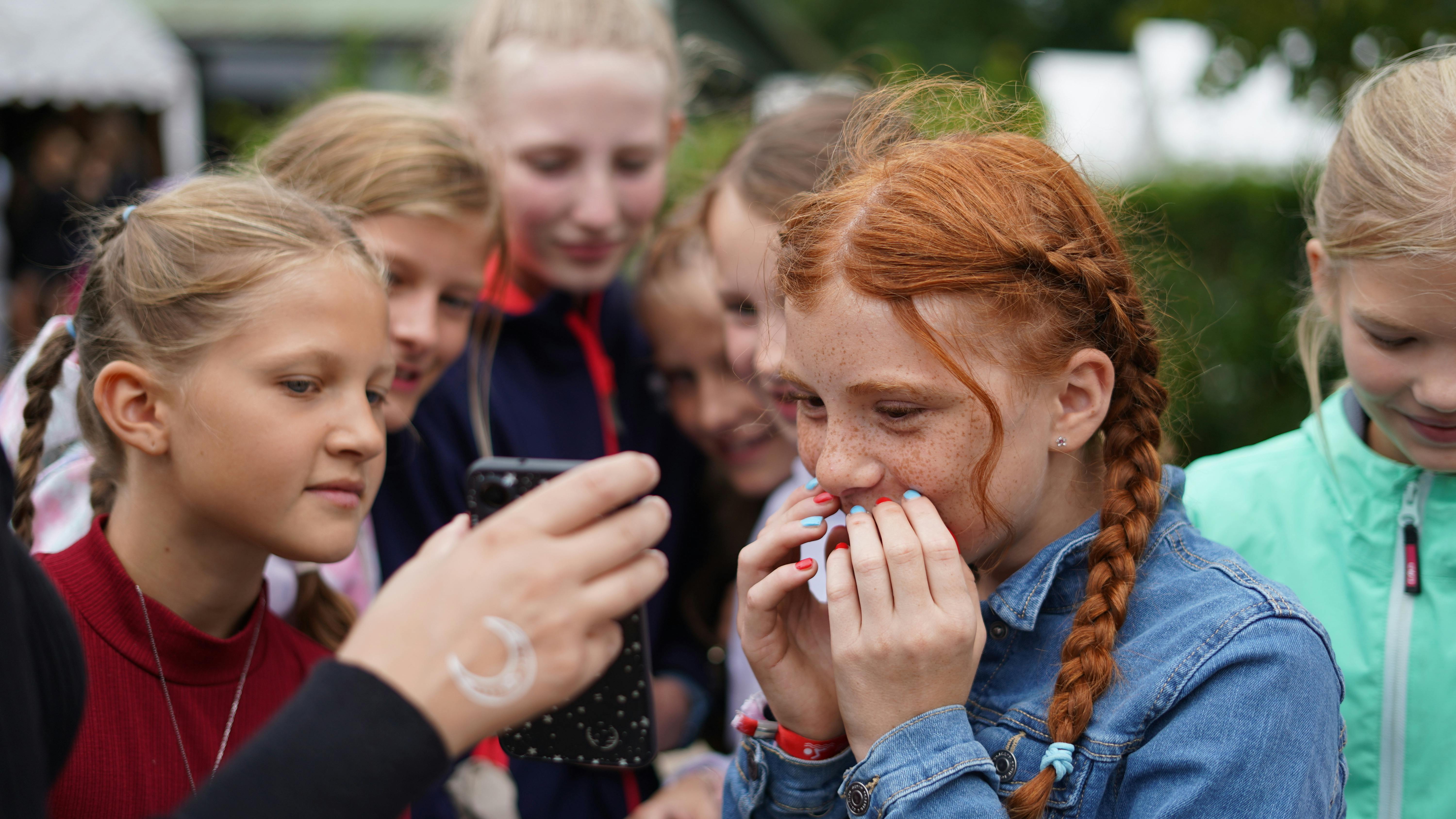 Mädchen schauen auf ein Handy, das ihnen hingehalten wird