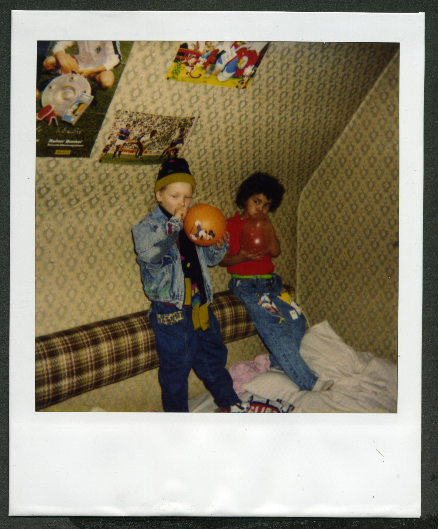 Wir sehen die Autorin in vermutlich ihrem Kinderzimmer im Alter von sieben Jahren. Neben ihr steht ein weißer Junge gleichen Alters und bläst einen orangenen Luftballon auf. 